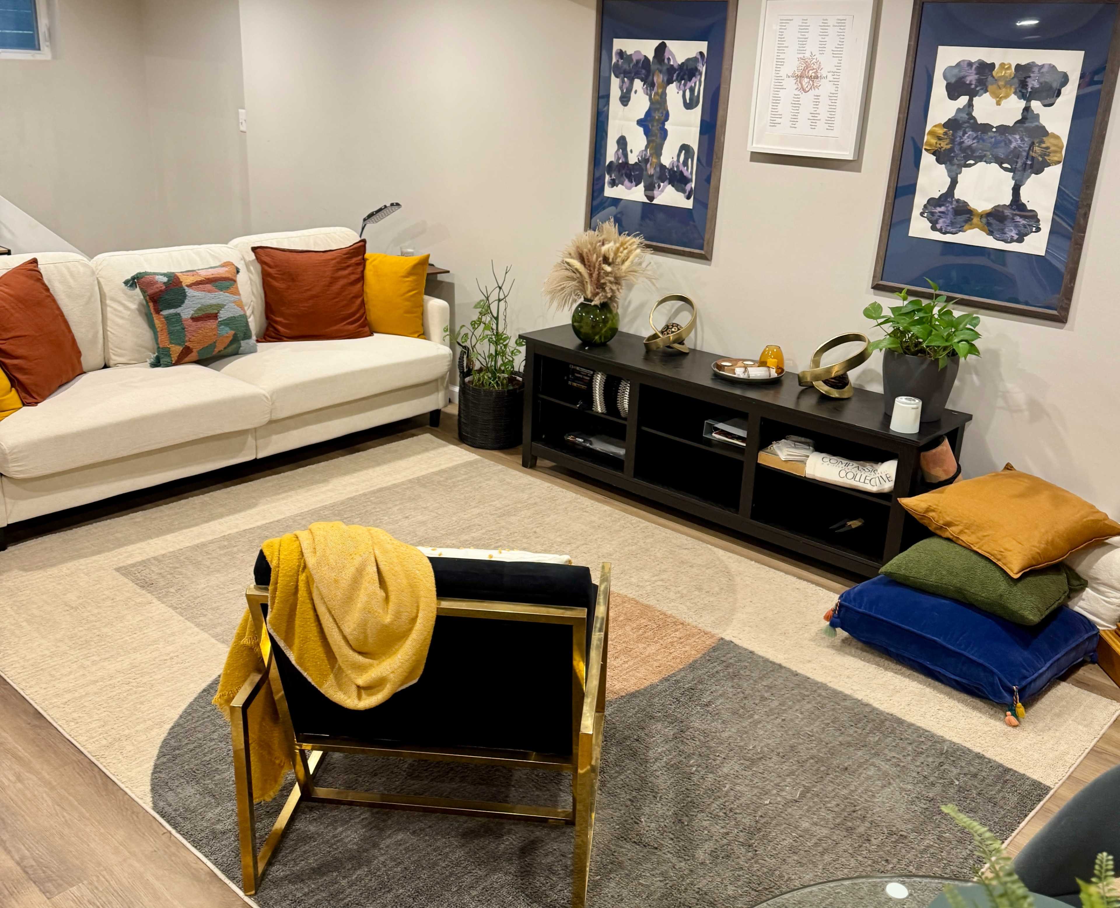 A cozy living room features a beige sofa with colorful pillows, a black media console, and a geometric rug, complemented by framed art on the walls.