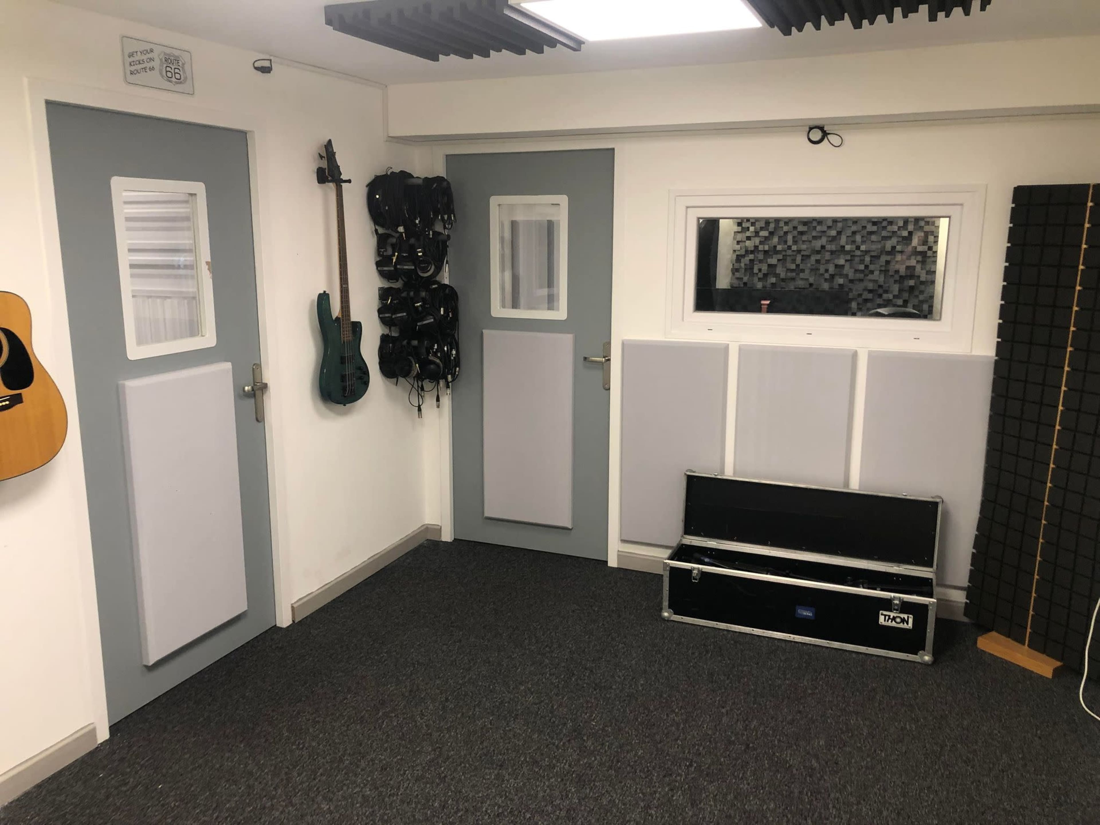 A soundproofed music studio with two doors, a window, various musical instruments hanging on the wall, and sound-absorbing panels.