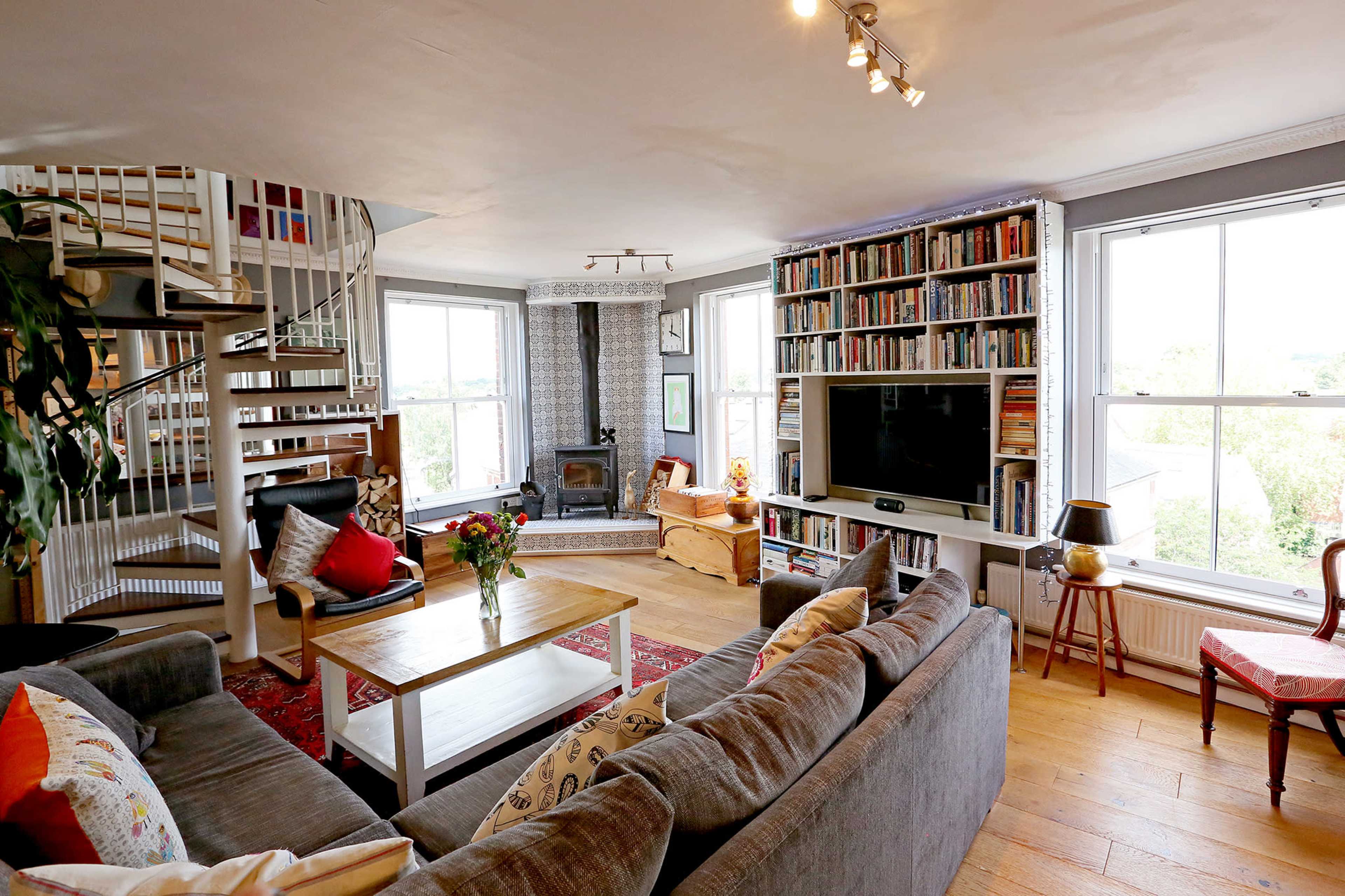 The living room features a gray sectional sofa, a wooden coffee table, built-in bookshelves, a spiral staircase, large windows, and a fireplace.
