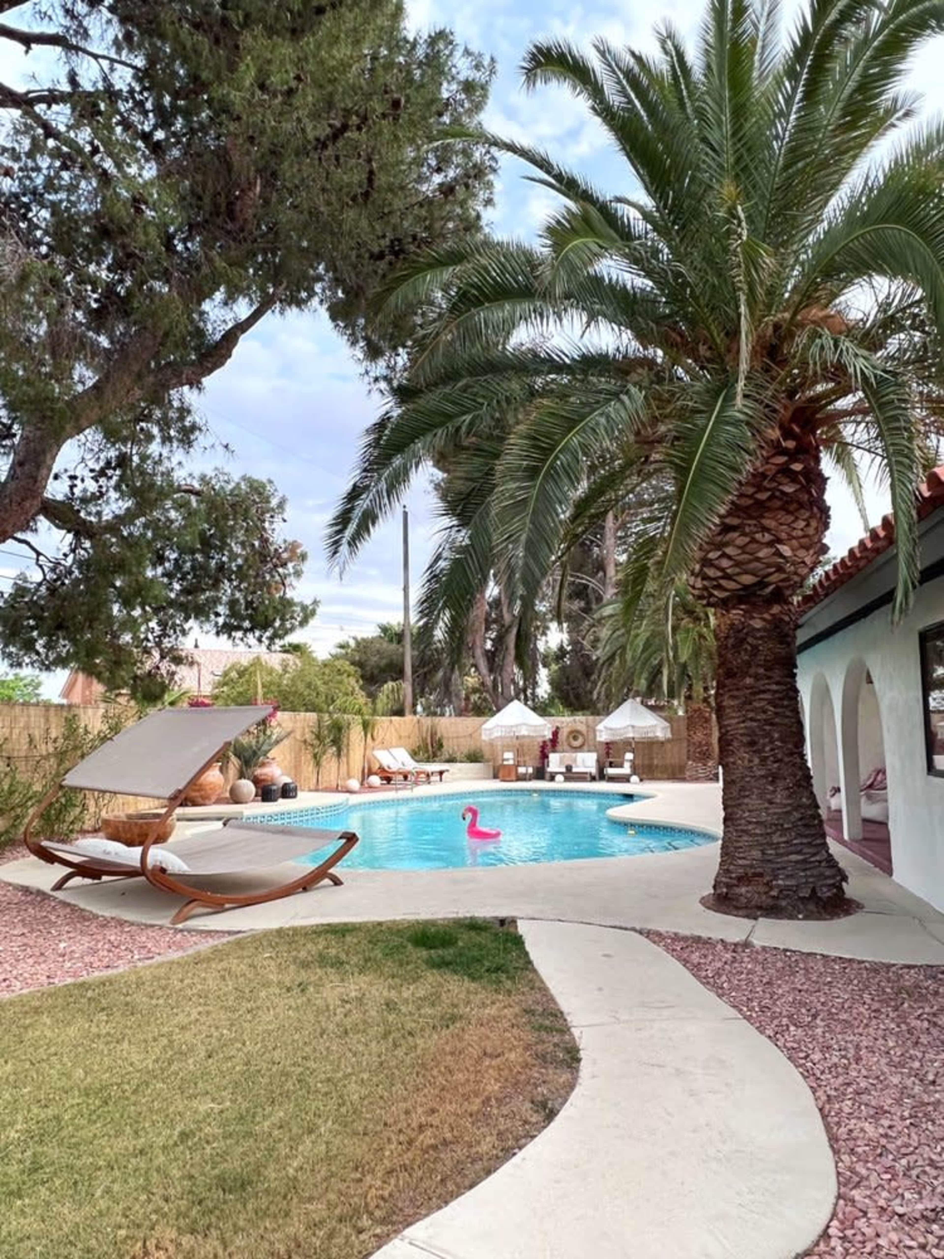 A pool area features a palm tree, lounge chairs, and a pink flamingo float, surrounded by landscaped grass and pathways.