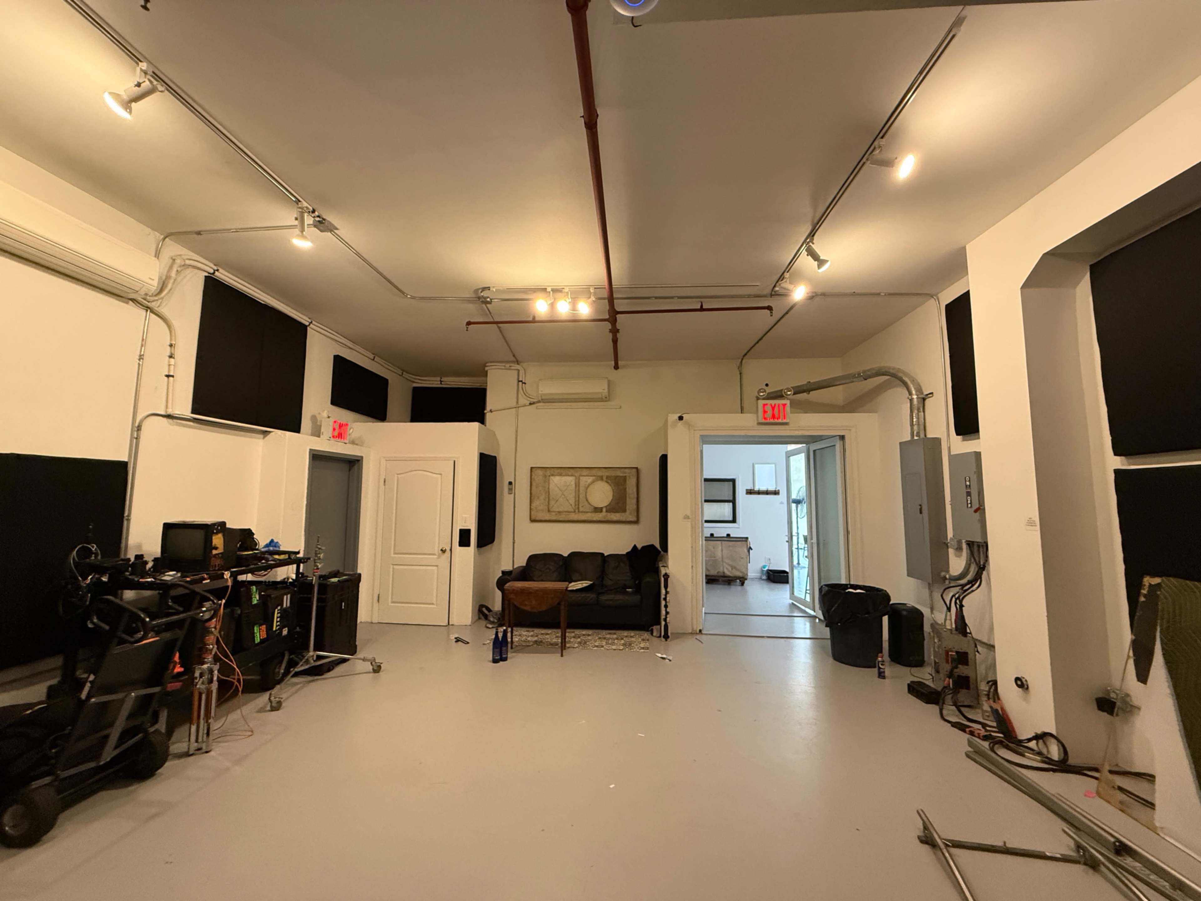 The image shows an empty room with a couch, a coffee table, and various equipment against the walls.