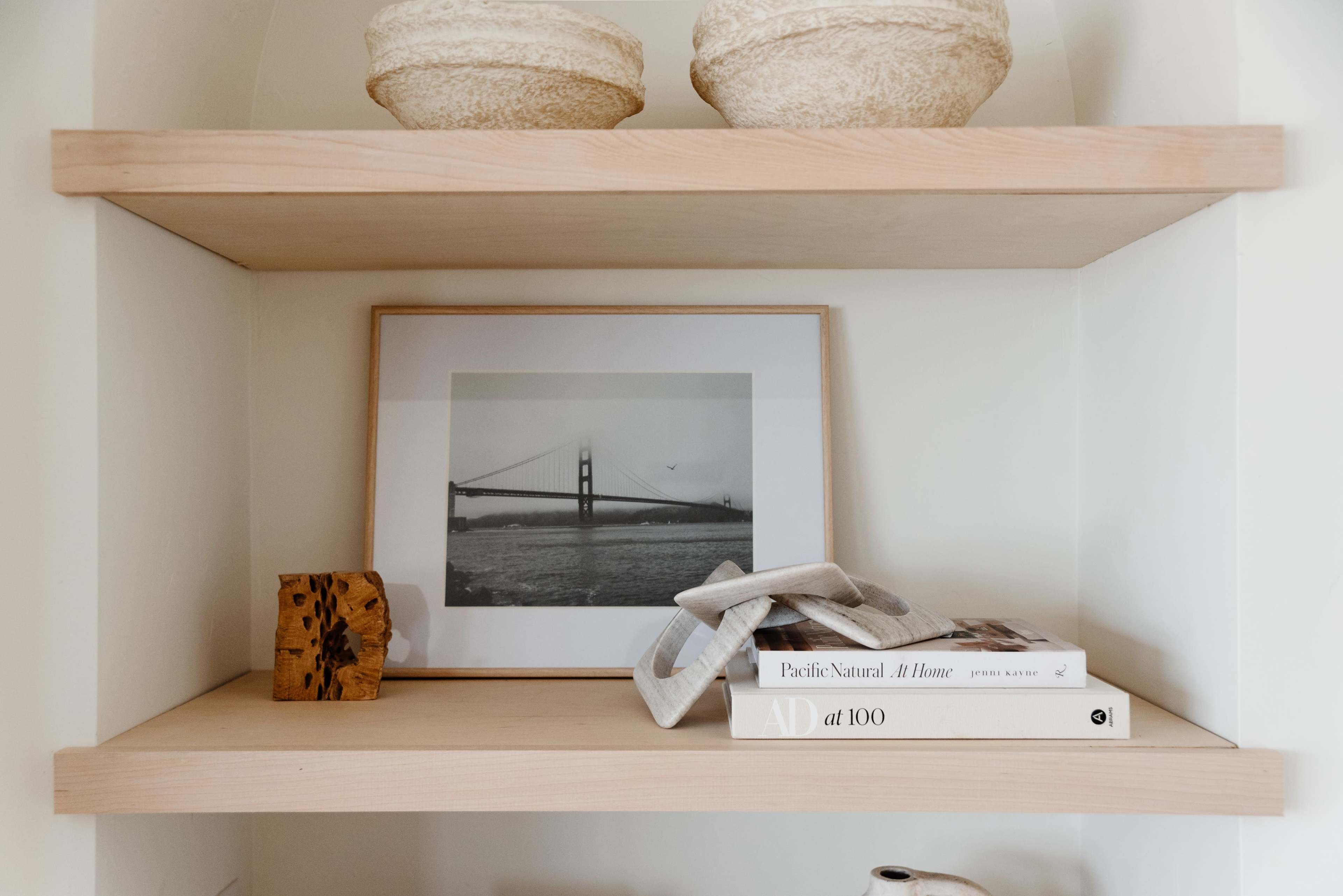 A wooden shelf displays a framed black-and-white photograph of a bridge, decorative bowls, a wooden block, and stacked books.