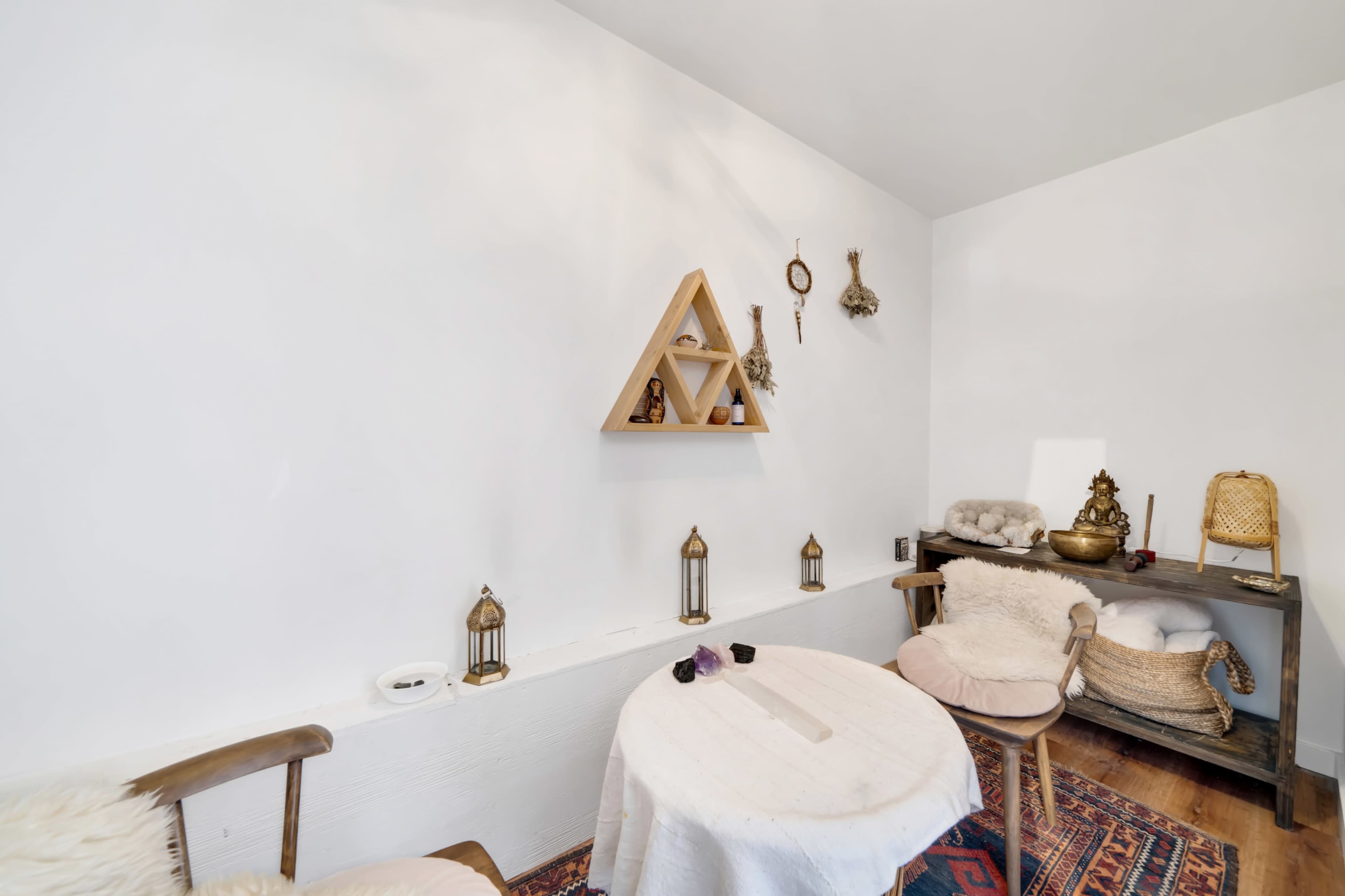 A minimalistic room features a small table with a decorative centerpiece, surrounded by two chairs and adorned with various hanging items on the white walls.