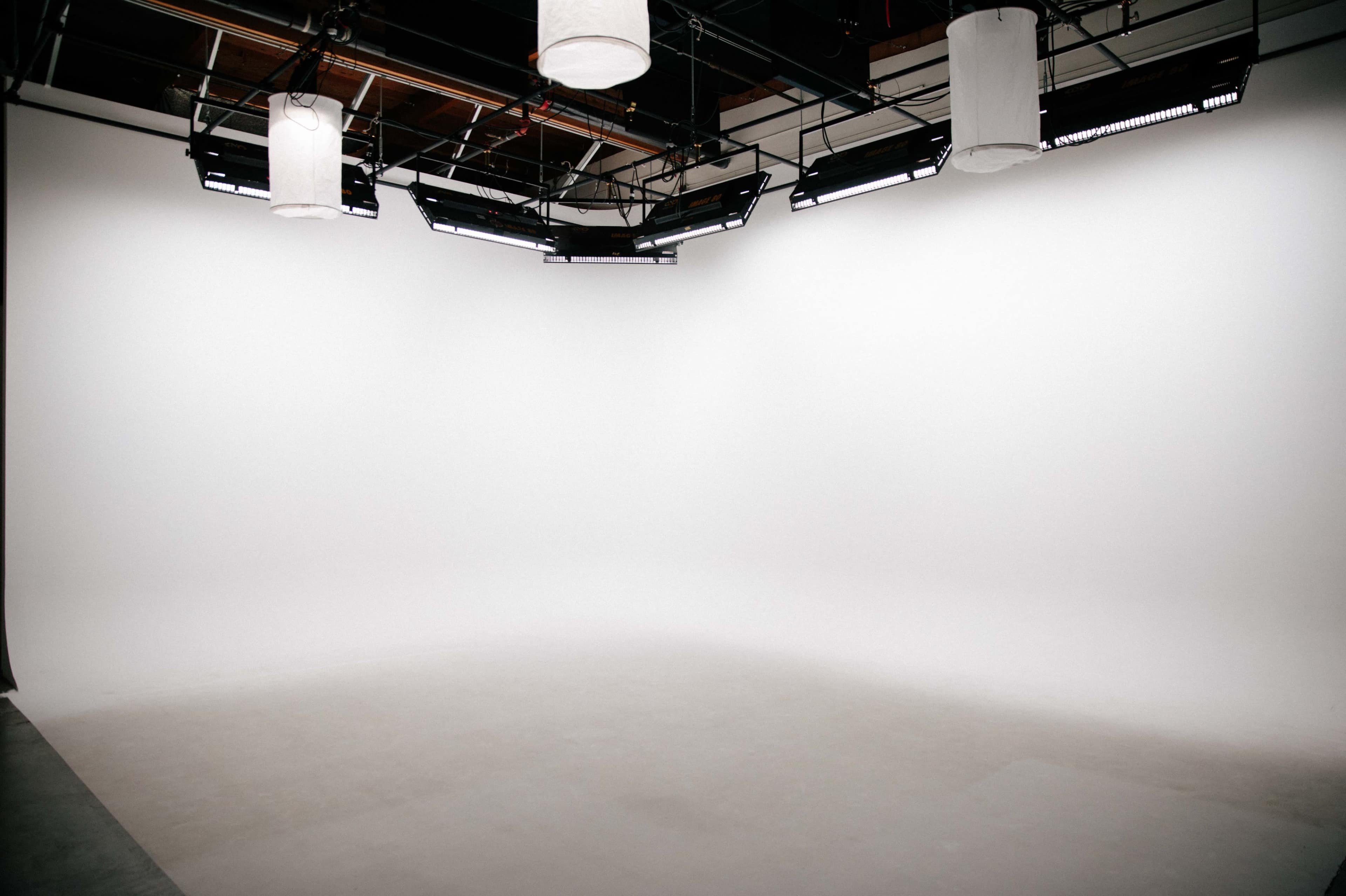 The image shows a photography studio with a white backdrop and several hanging lights.