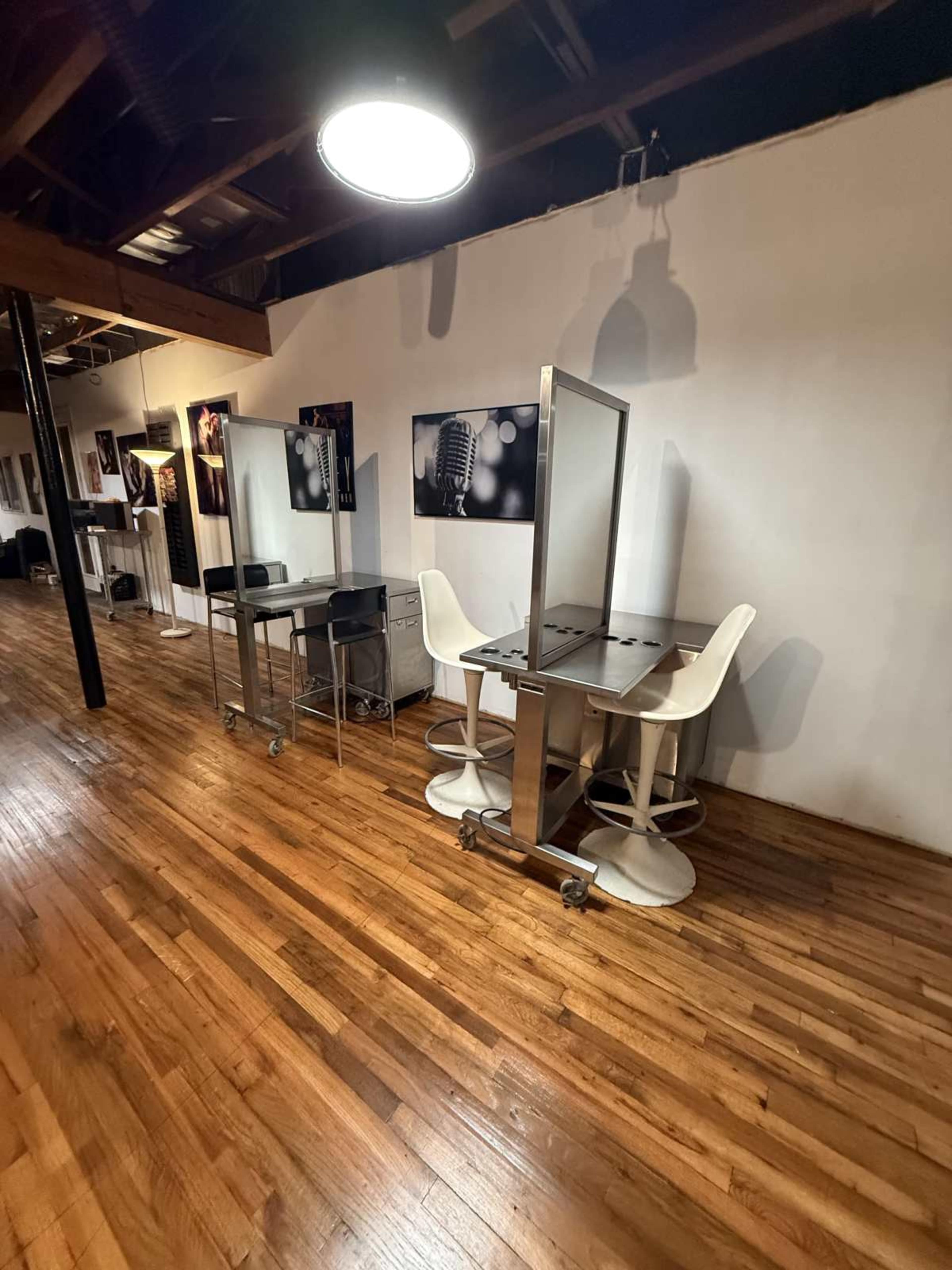 The image shows a studio space with wooden flooring, featuring two metal tables with chairs and photography backdrops on the walls.