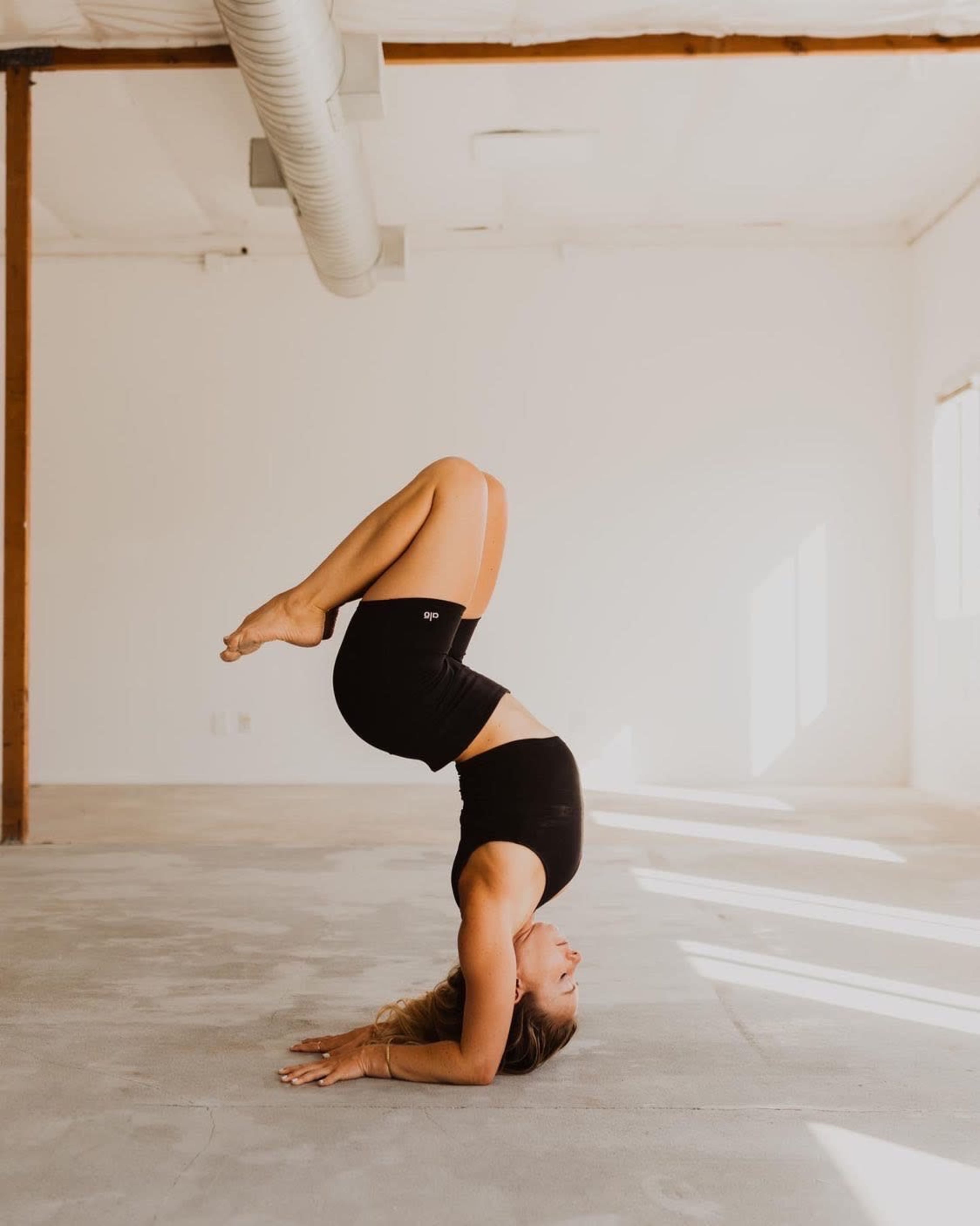 A person performs a headstand on a concrete floor in a well-lit room.