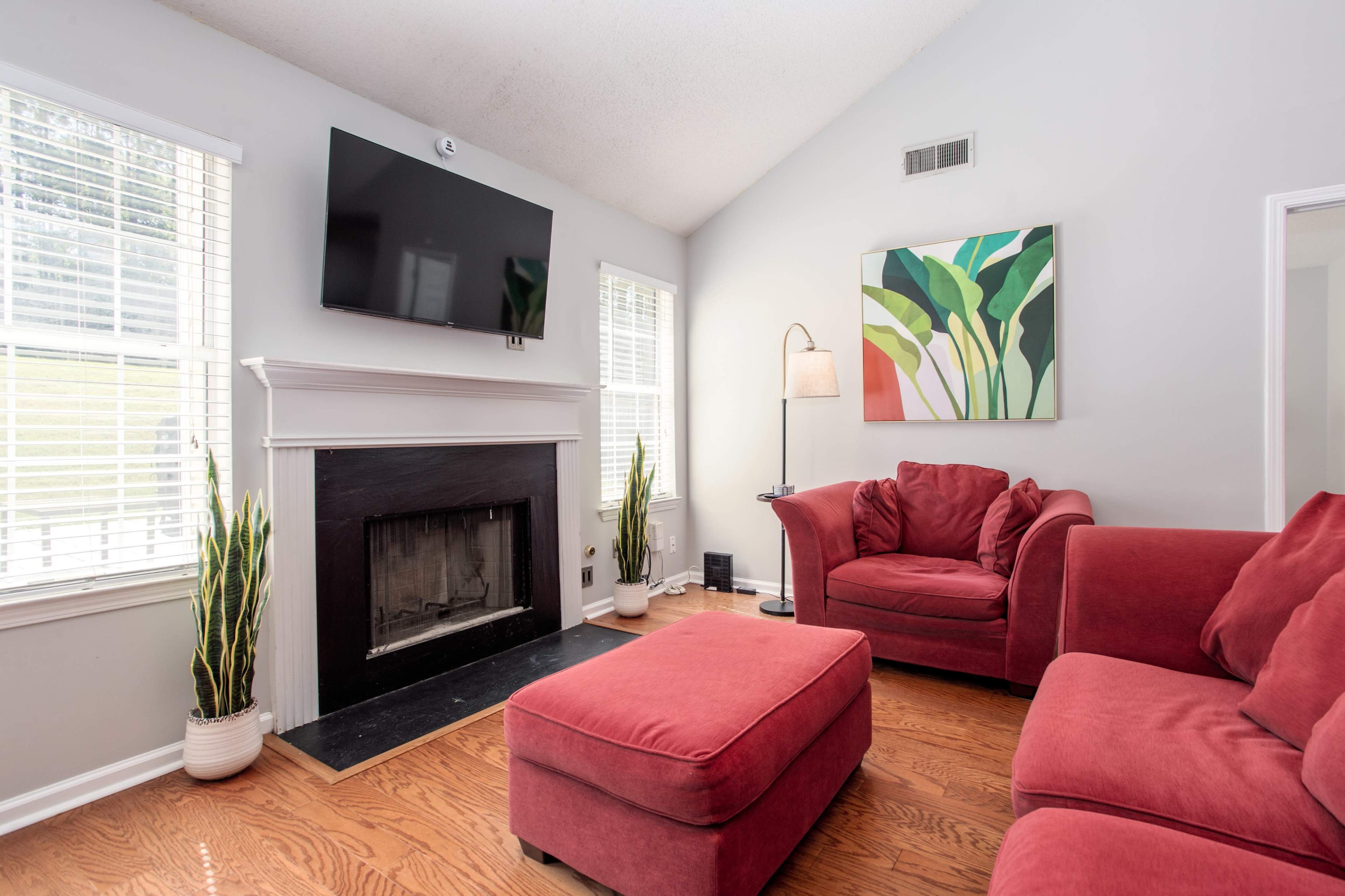 The living room features a red sofa set, a mounted TV above a black fireplace, and an abstract painting on the wall.