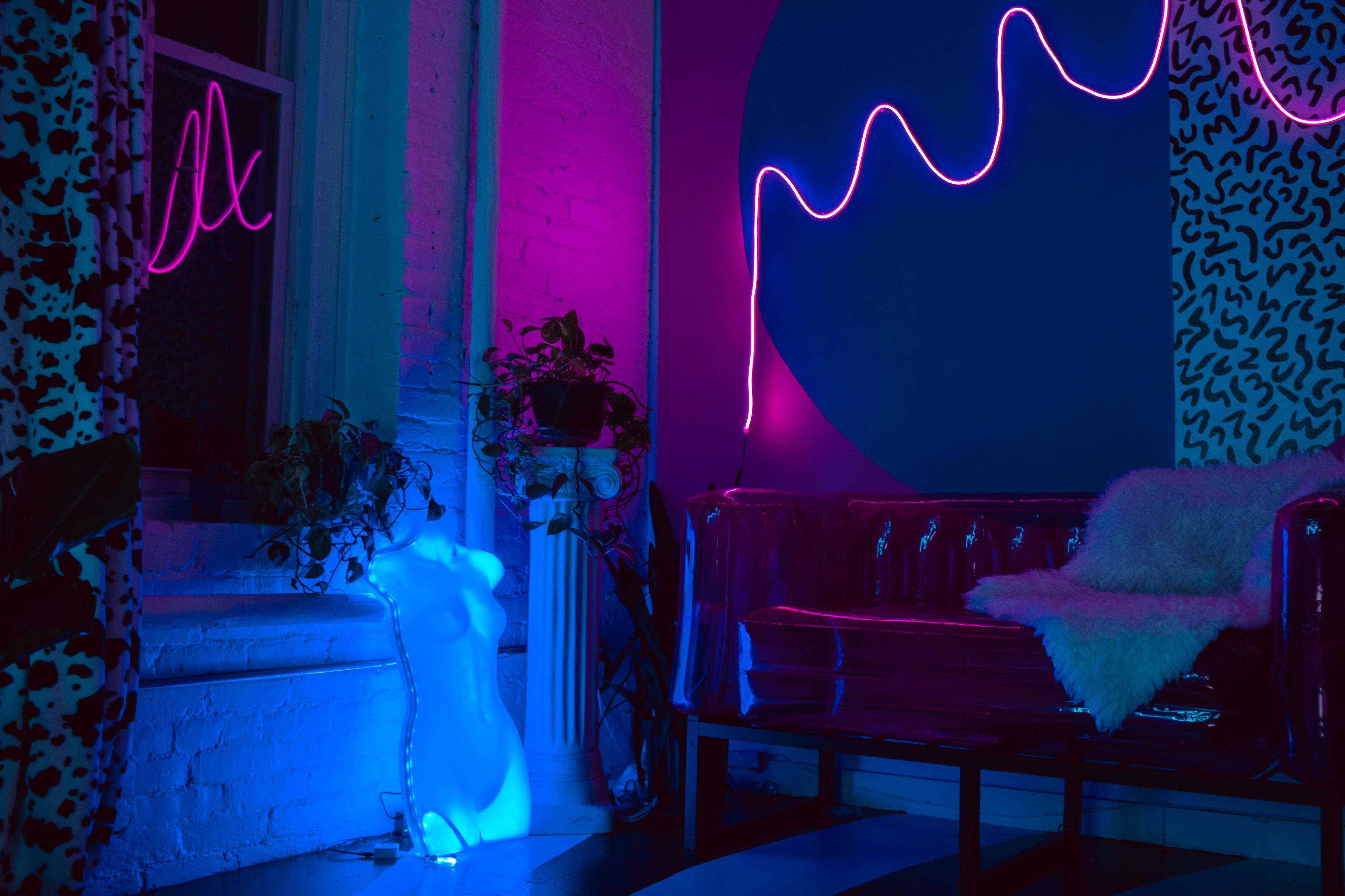 The scene features a brightly lit room with neon pink and blue lights, displaying a mannequin beside a transparent couch and a large circular blue wall design.