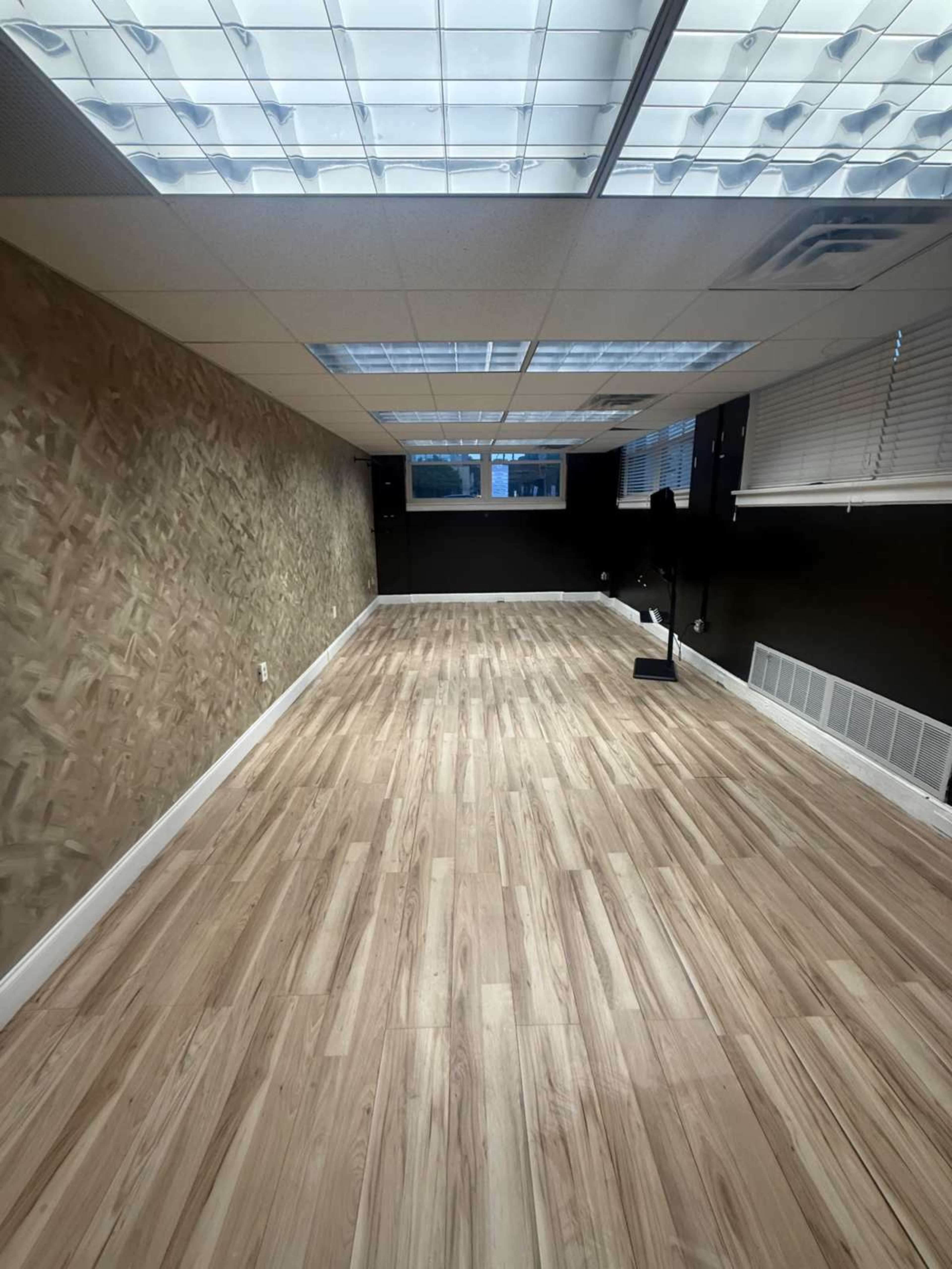 The image shows a spacious room with wooden flooring, a textured wall, and large skylights providing natural light.