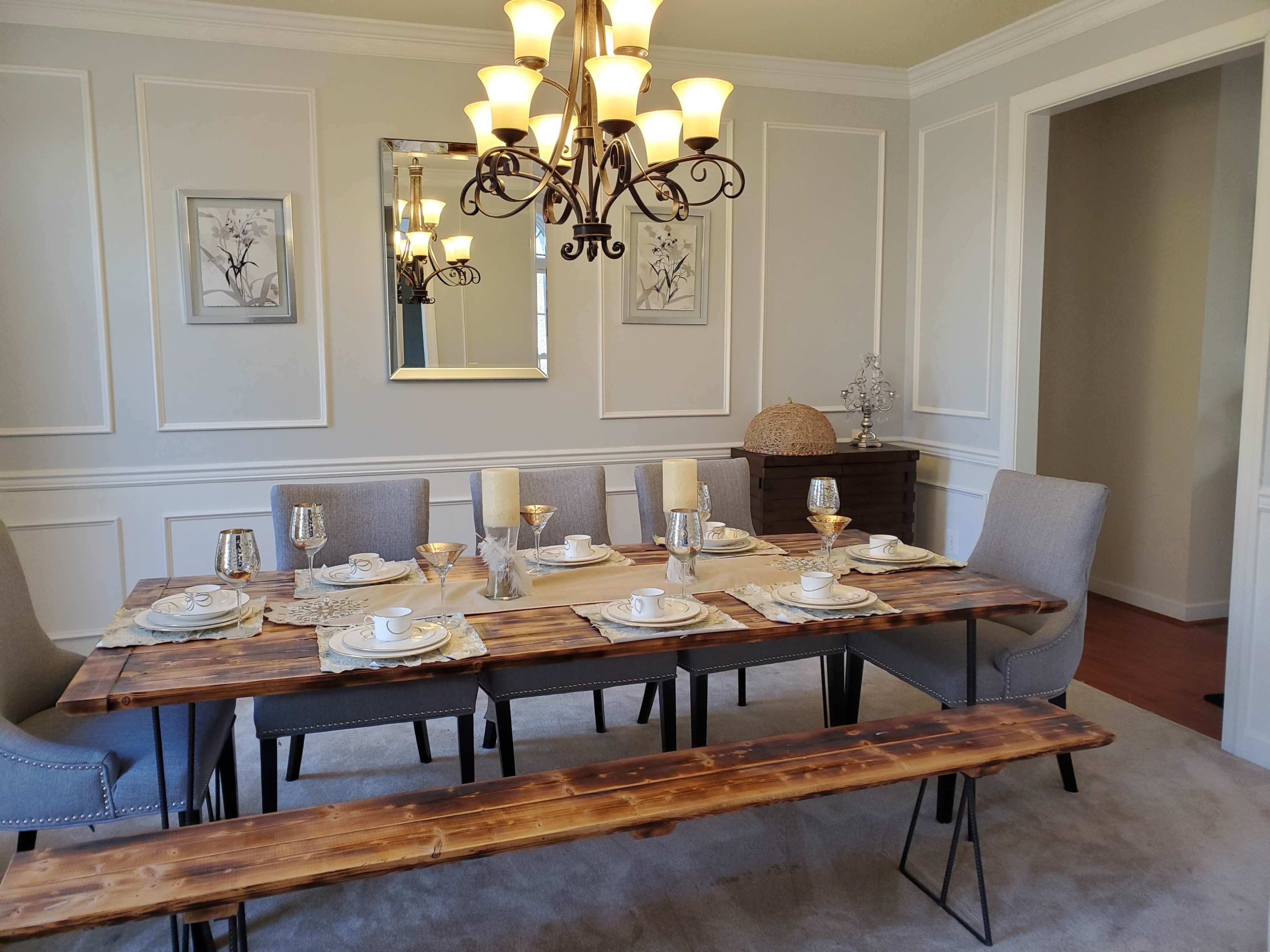 The dining room features a wooden table set for a meal, surrounded by gray chairs and illuminated by a chandelier.