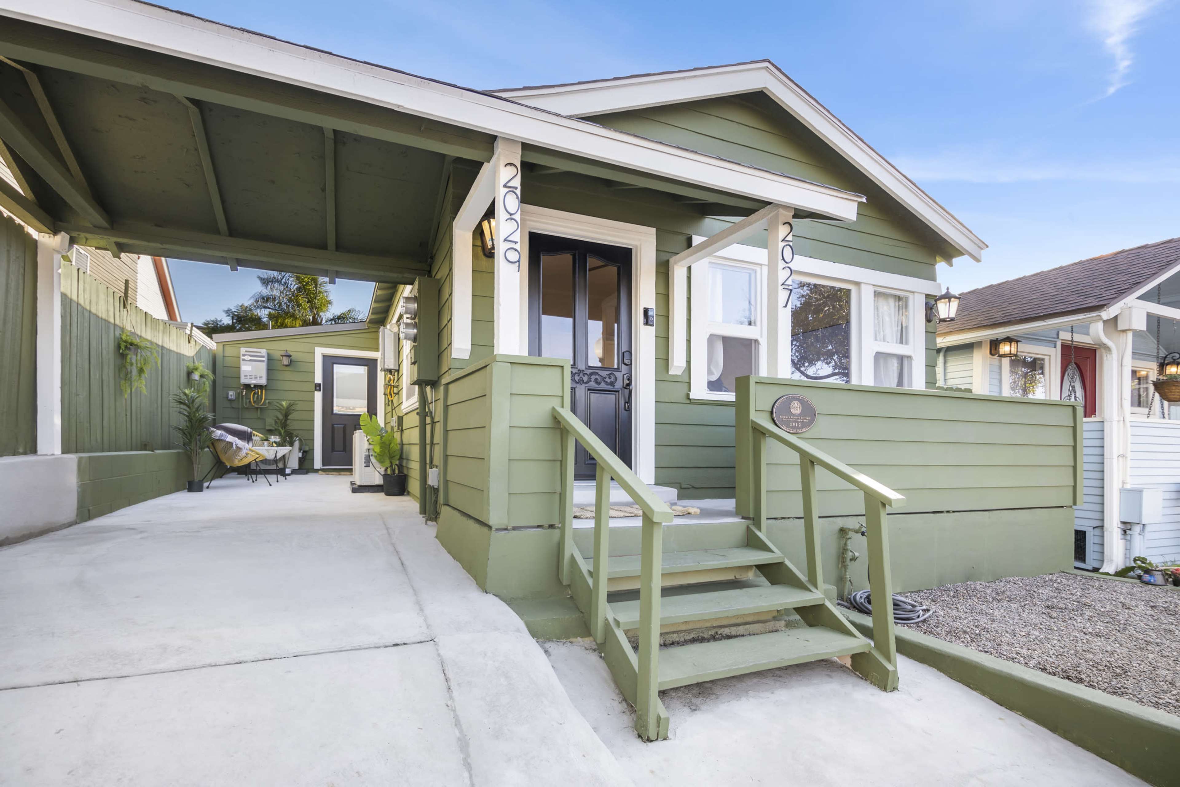 A green house with a covered porch and stairs leading up to the front door, situated on a clear day.