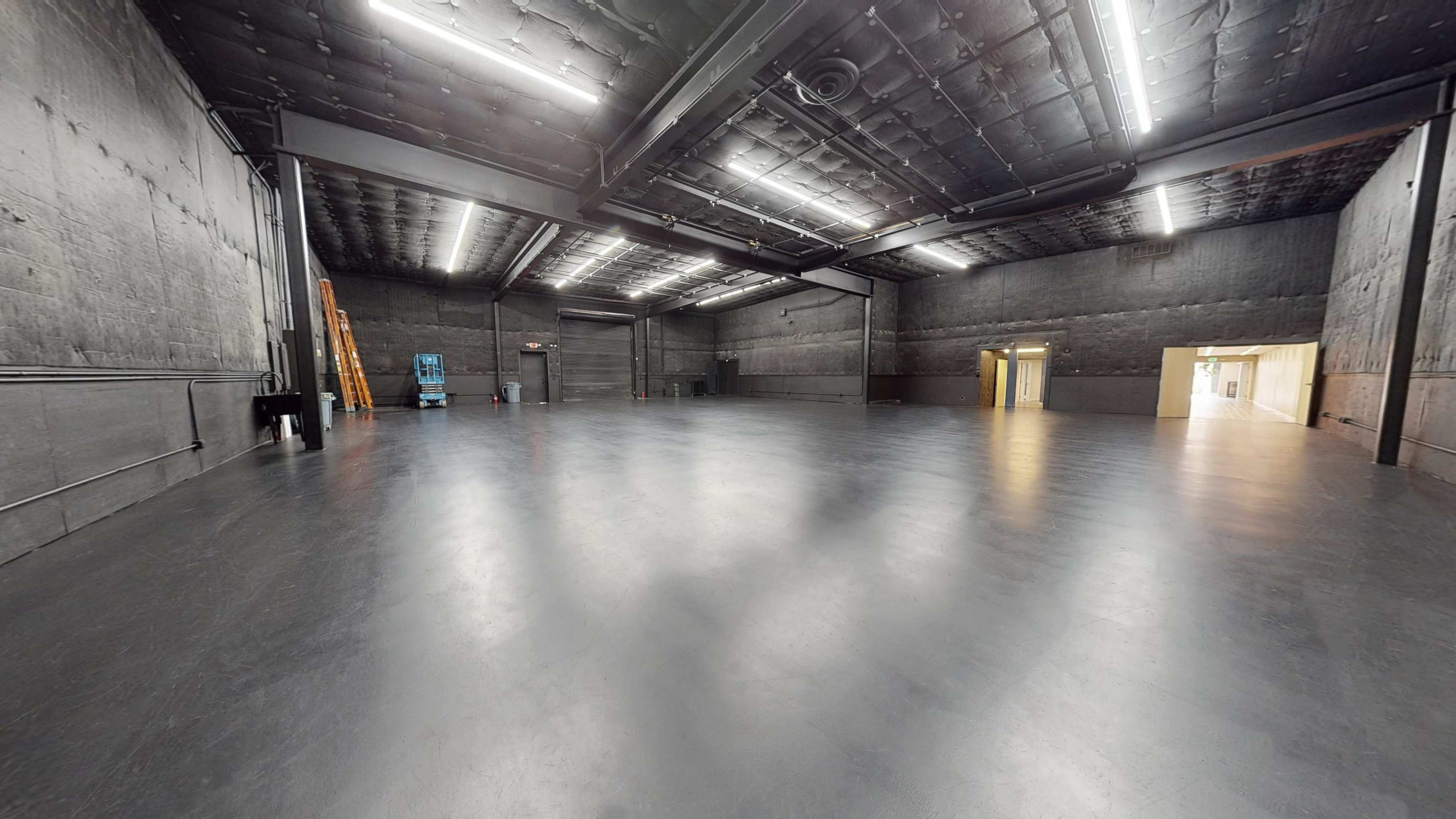The image shows a large, empty industrial space with black walls, a smooth floor, and overhead lighting.