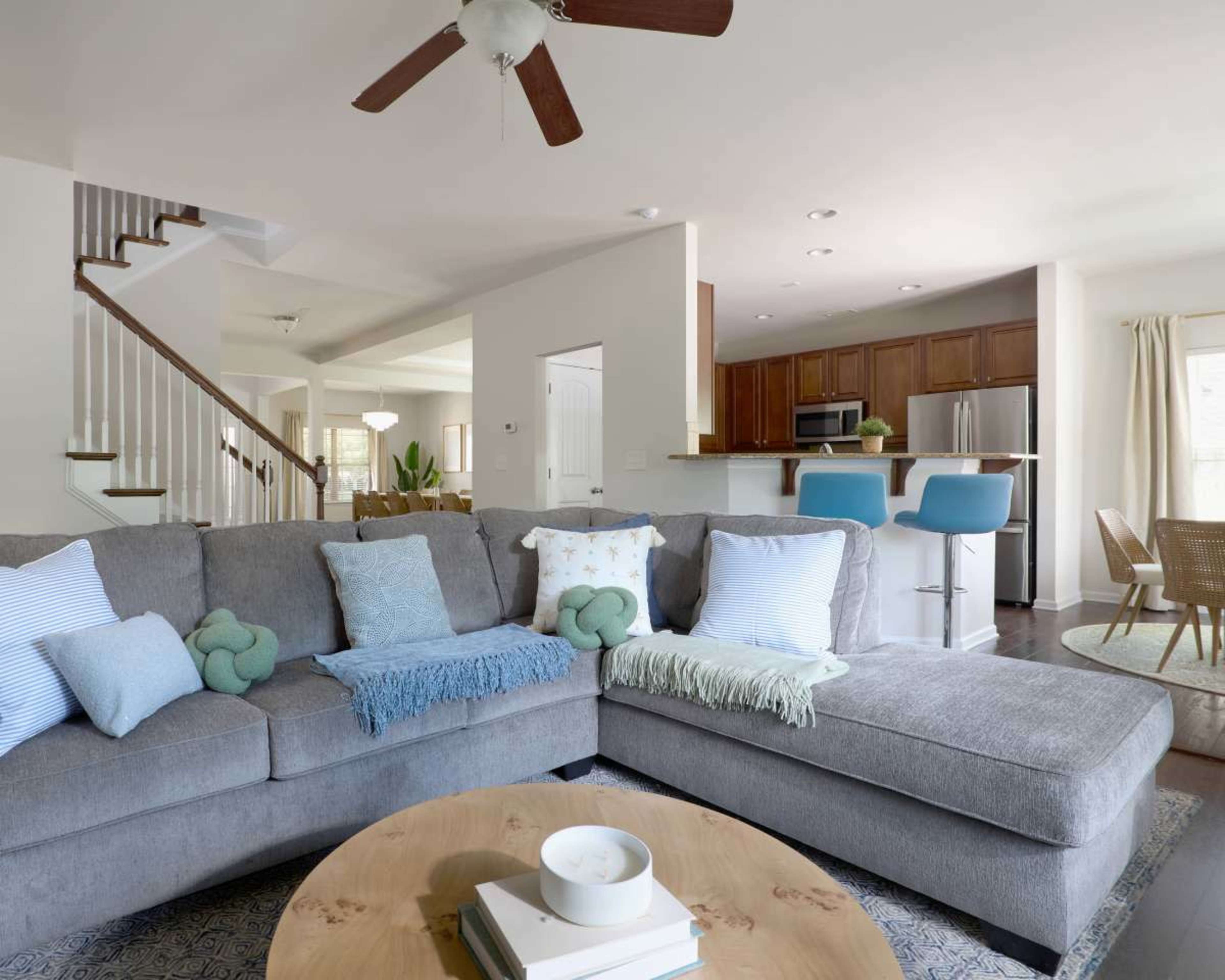 A spacious living room features a large gray sectional sofa, a wooden coffee table, and an open plan layout with a staircase leading to the upper level.
