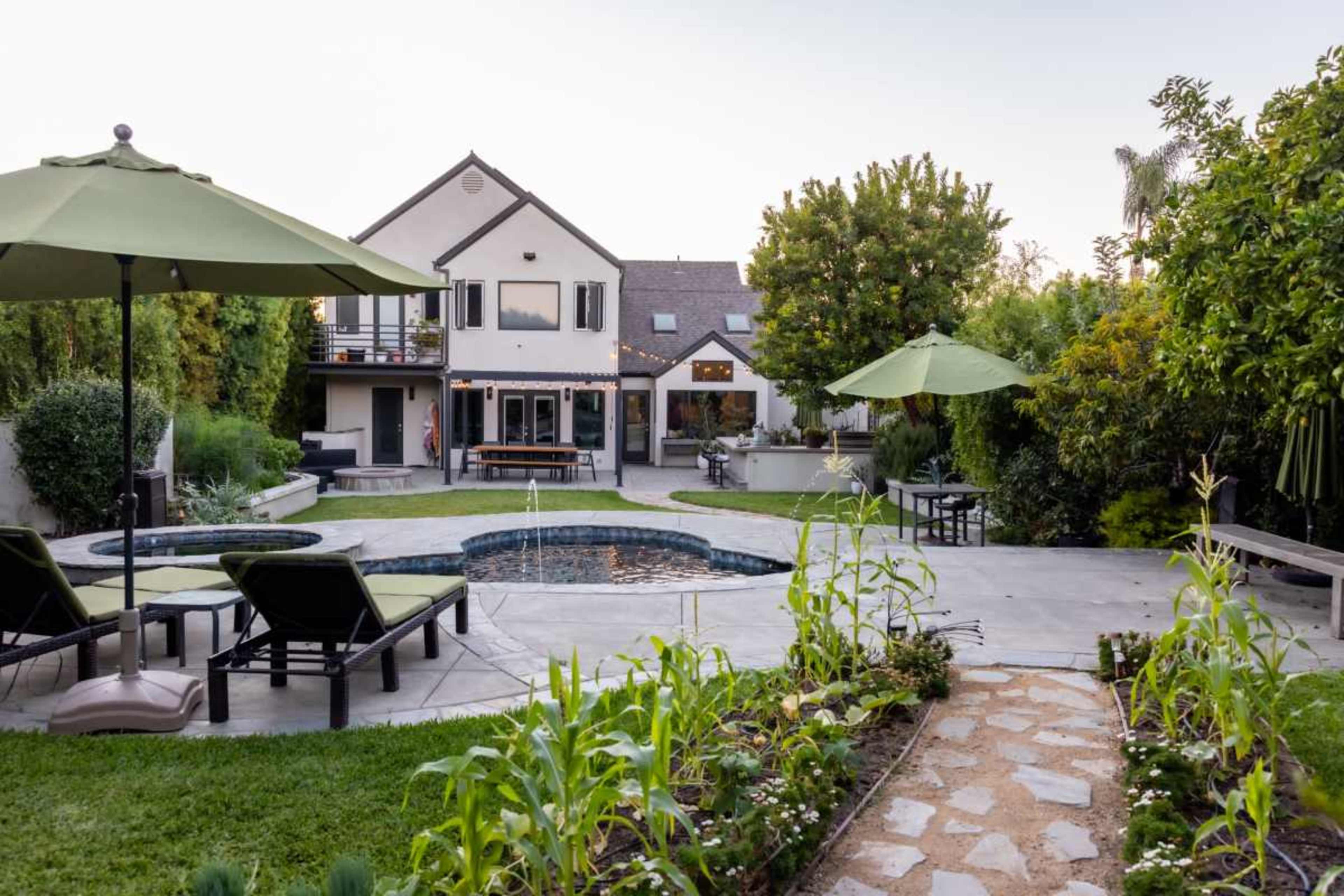 The image shows a backyard scene featuring a swimming pool, lounge chairs, and patio umbrellas, with a house and garden in the background.