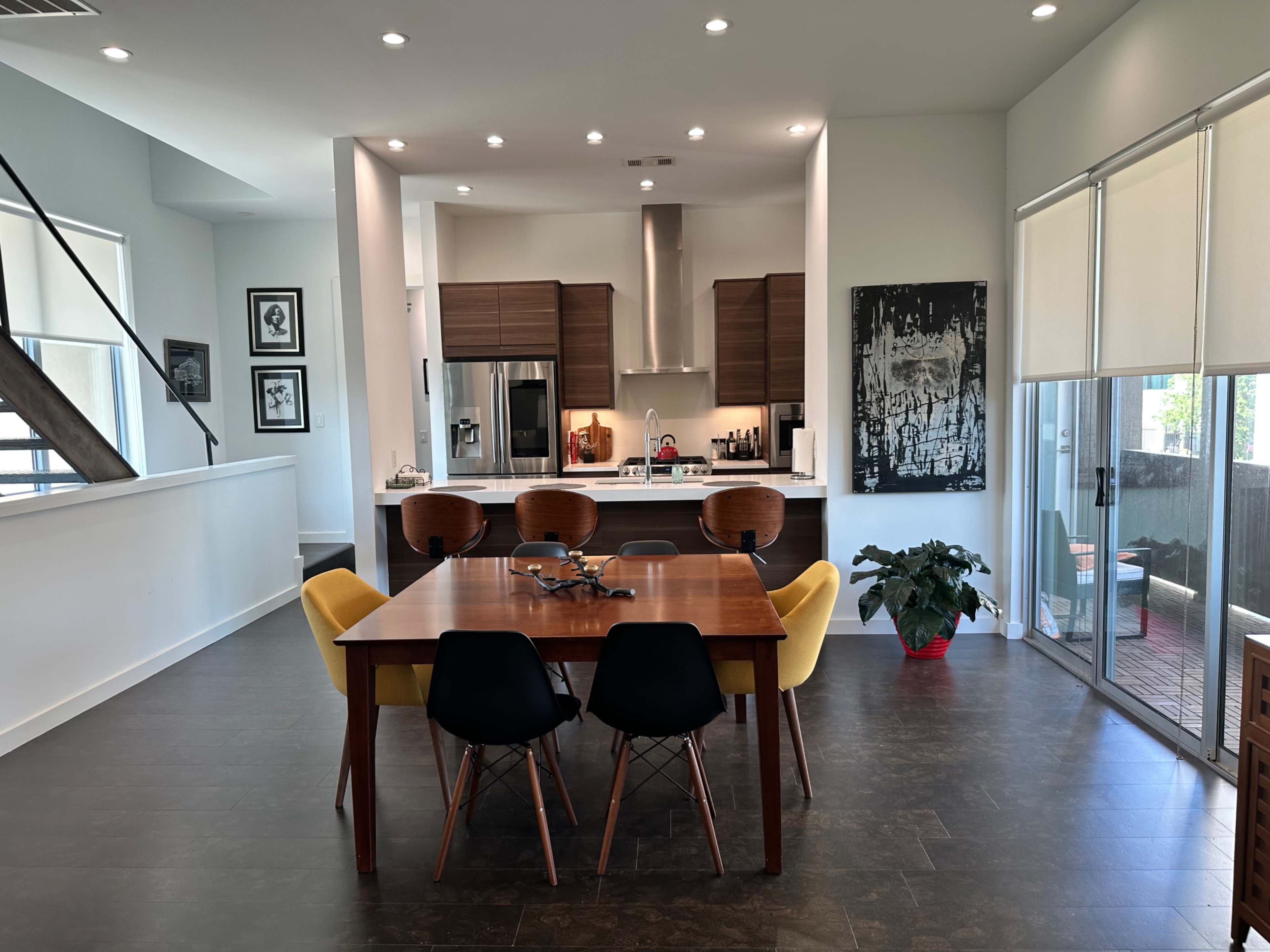 A modern dining area features a wooden table surrounded by six chairs, with an open kitchen visible in the background.