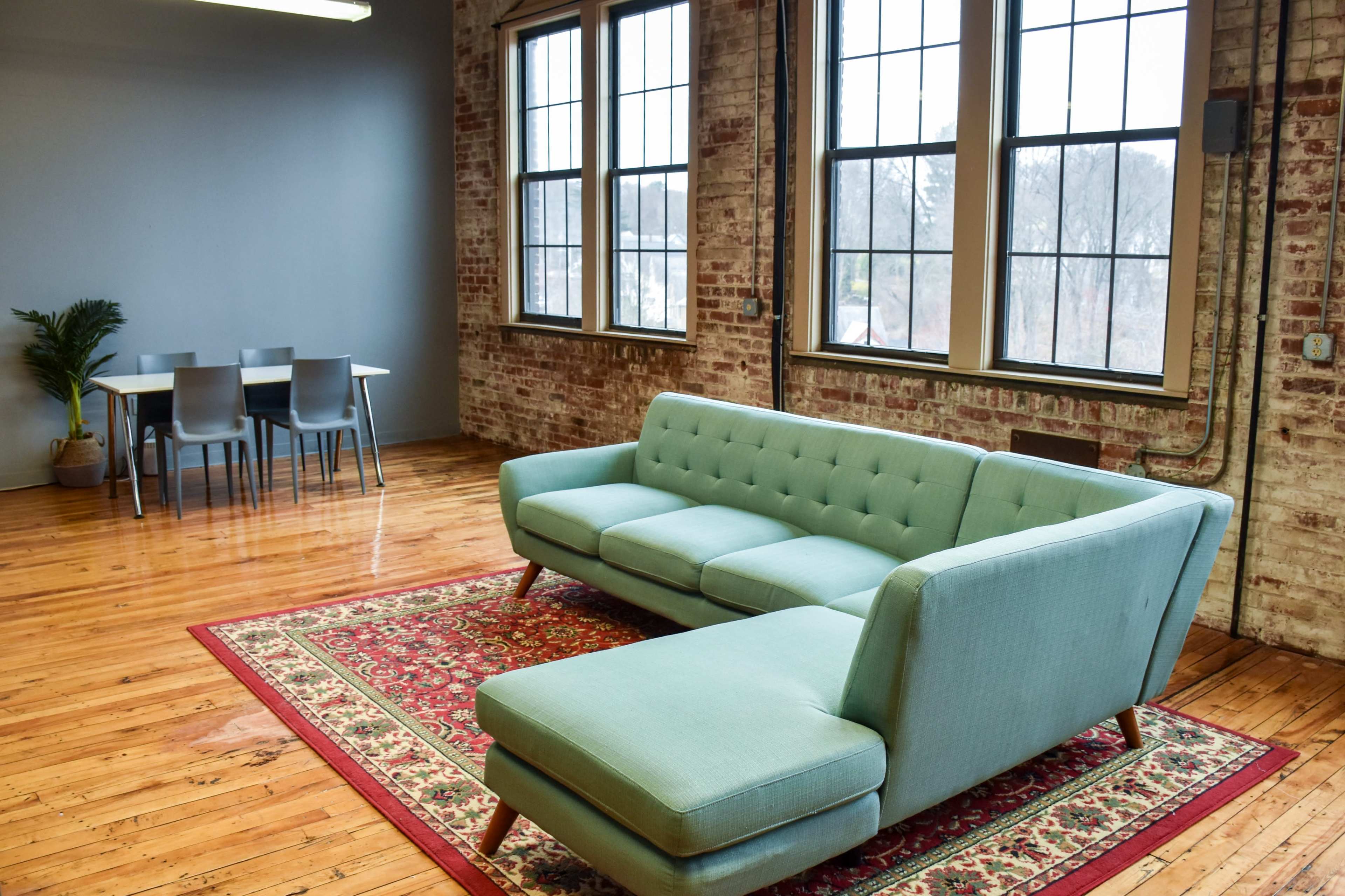A modern living space with a light blue sectional sofa, a patterned rug, and a dining table with chairs against a brick wall.