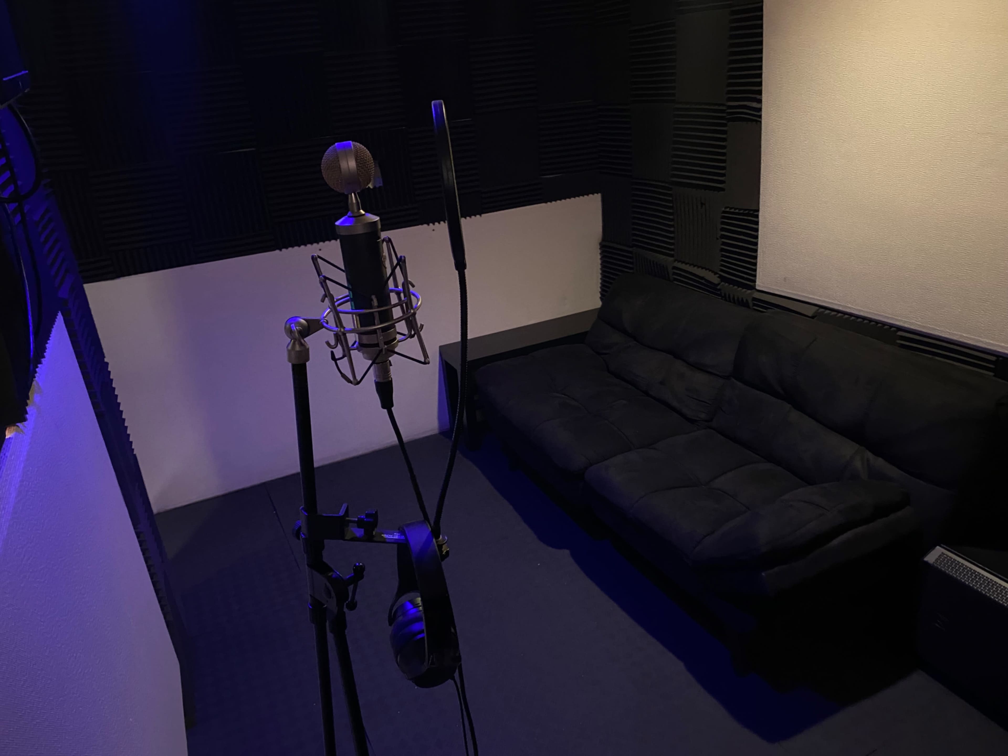 A small recording studio with a microphone on a stand and a black couch against the wall.