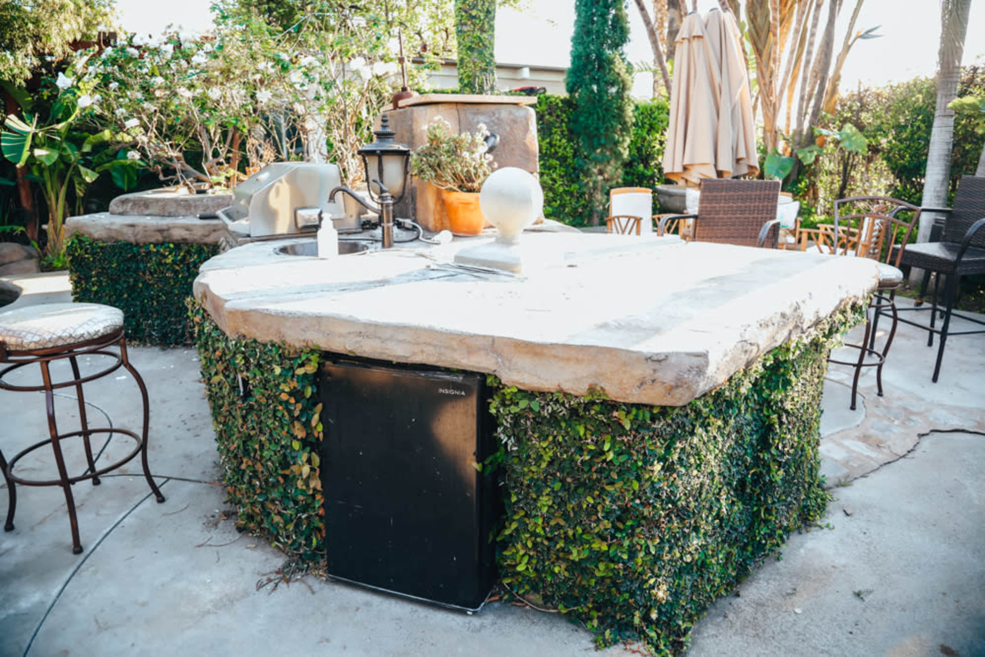 An outdoor kitchen island surrounded by lush greenery and seating areas.