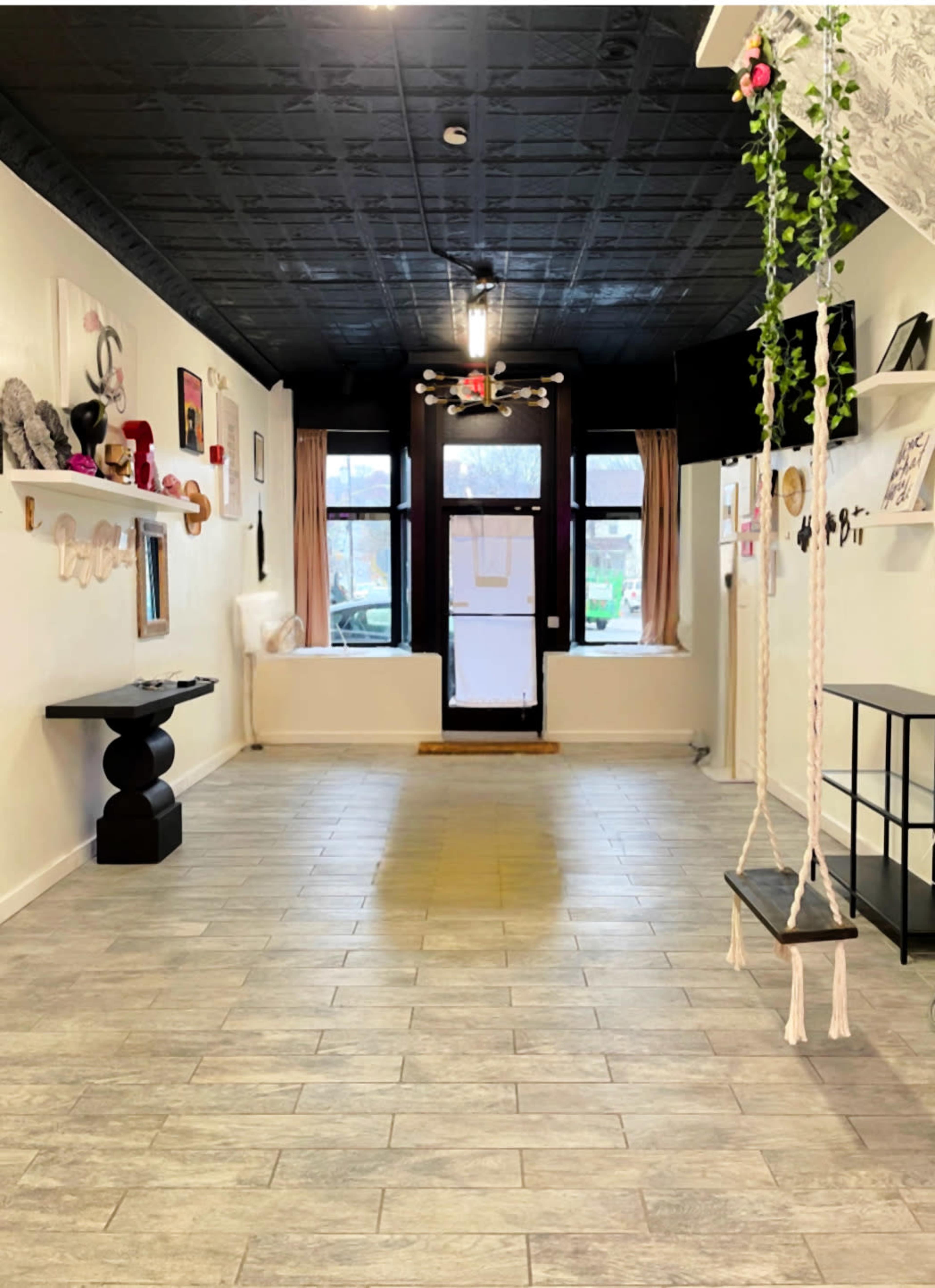 The image shows a vacant interior space with gray tile flooring, white walls adorned with various artworks, and a swing suspended from the ceiling near the entrance.