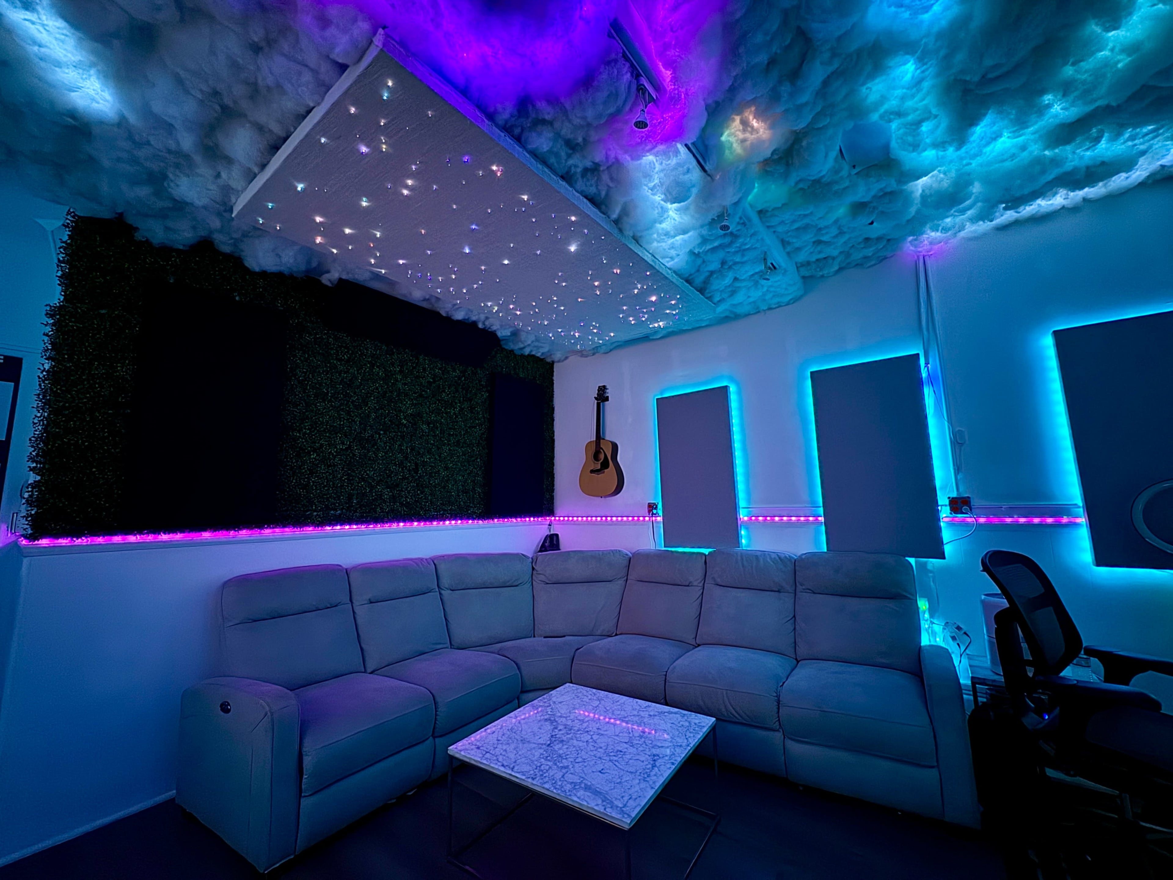 The image shows a modern lounge area featuring a sectional couch, a marble coffee table, and a ceiling designed with clouds and ambient lighting that creates a starry effect.