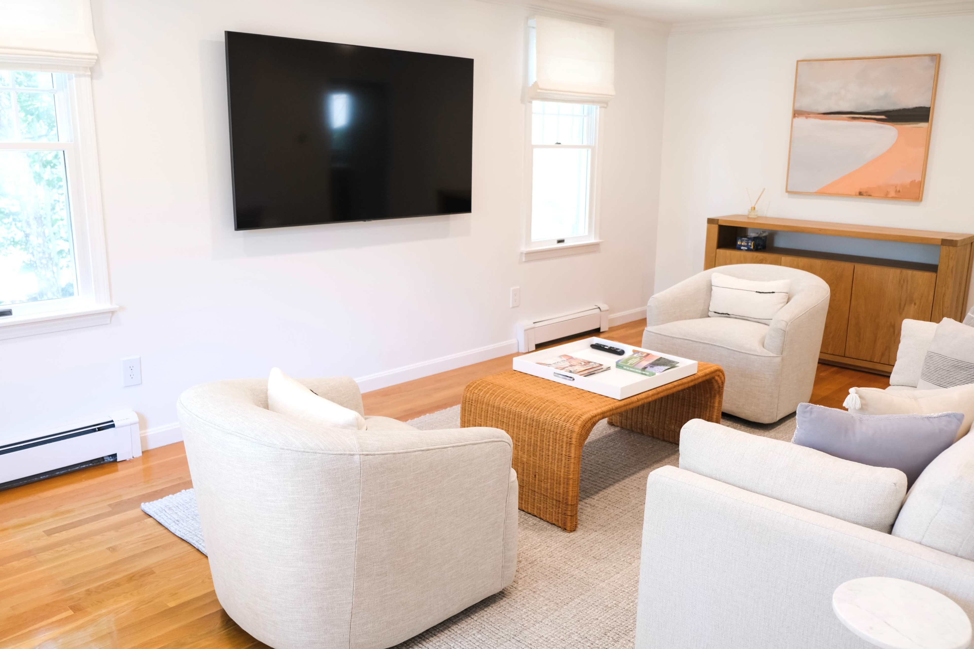 A sitting area features two light-colored chairs facing a coffee table, with a large wall-mounted TV and a piece of art hanging above.