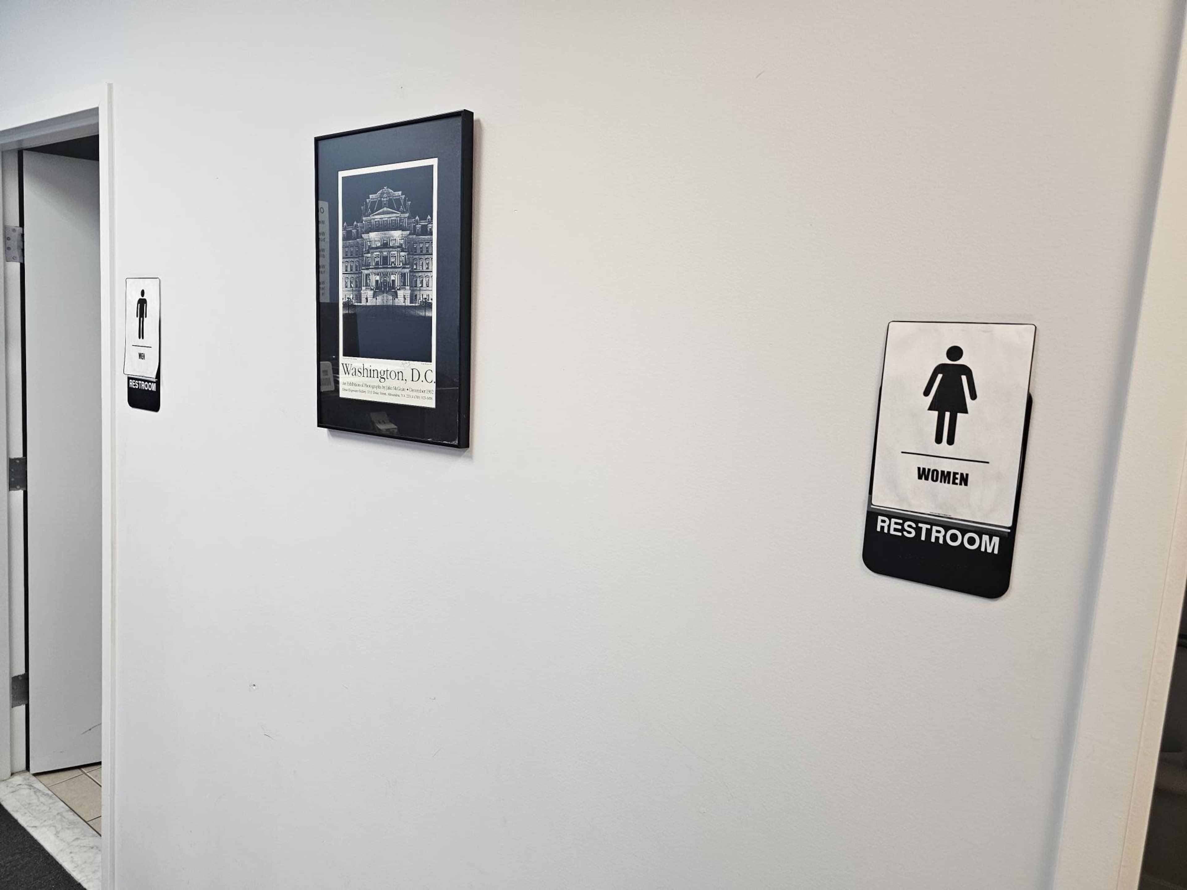 A hallway with a framed black-and-white photograph of a building alongside signs indicating the women's restroom on the wall.