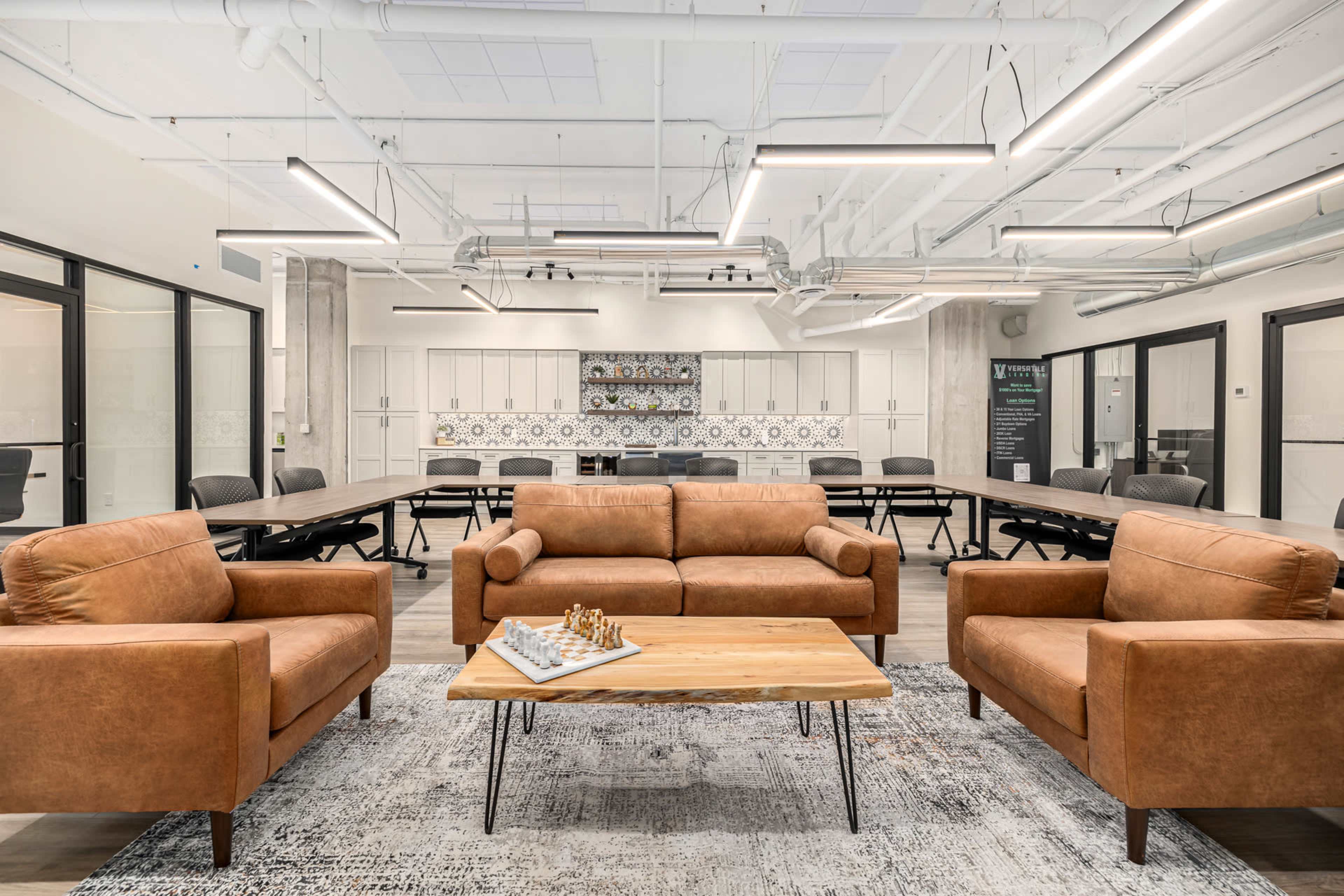 The image shows a modern office space featuring brown leather sofas, a wooden coffee table, and a large conference table surrounded by black chairs.