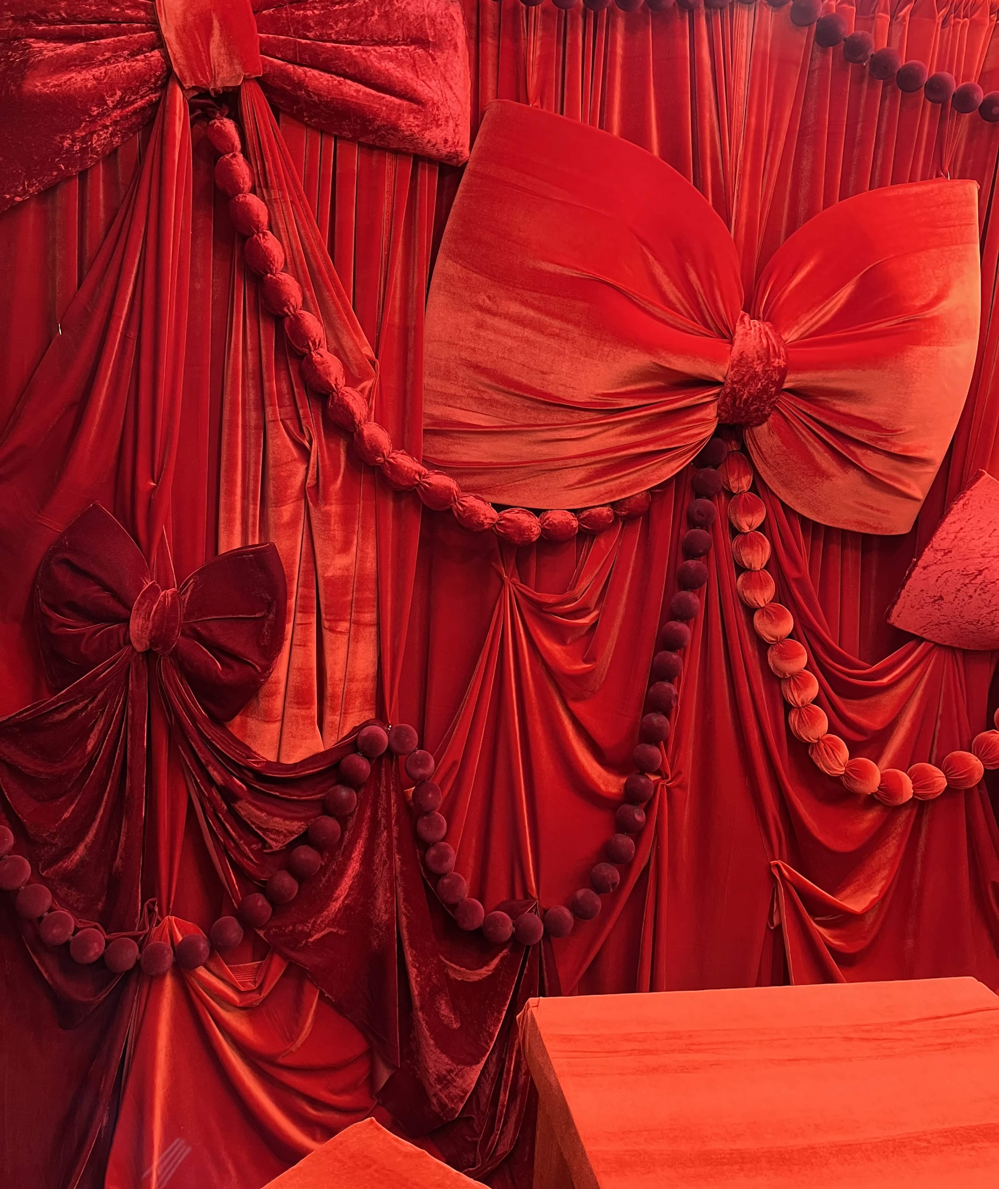 The scene features a wall draped in red fabric with large bows and decorative pom-poms.