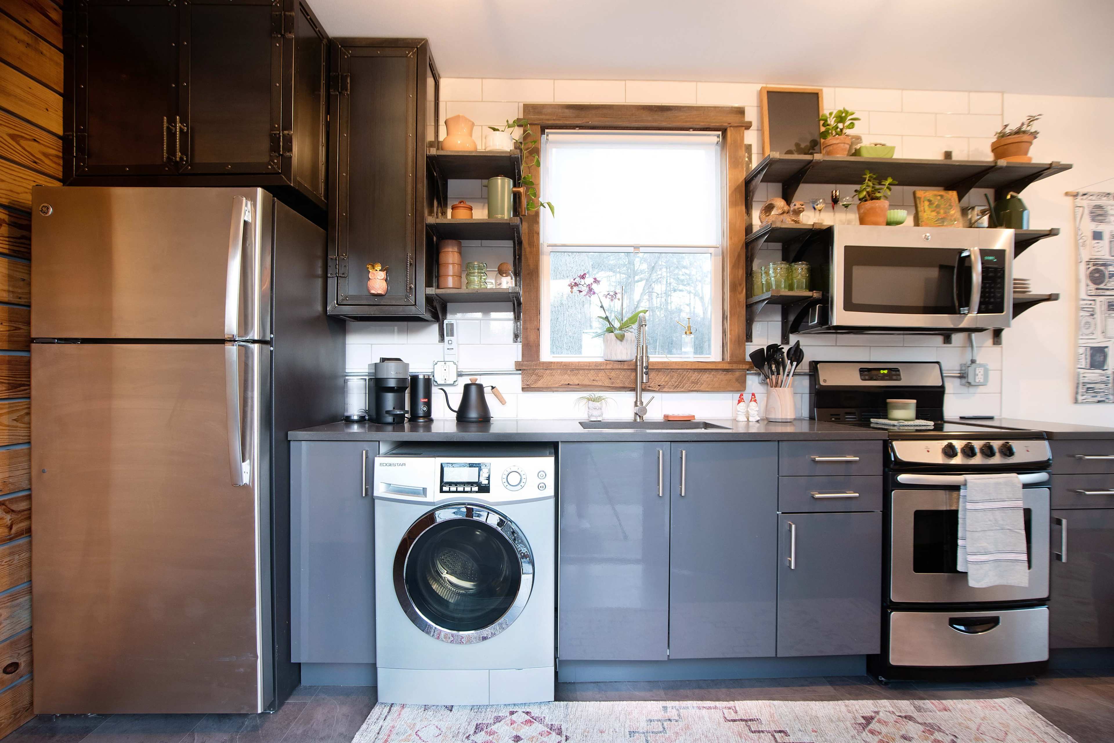 A modern kitchen features a stainless steel refrigerator, a washing machine, and sleek cabinetry with open shelves displaying various kitchen items.