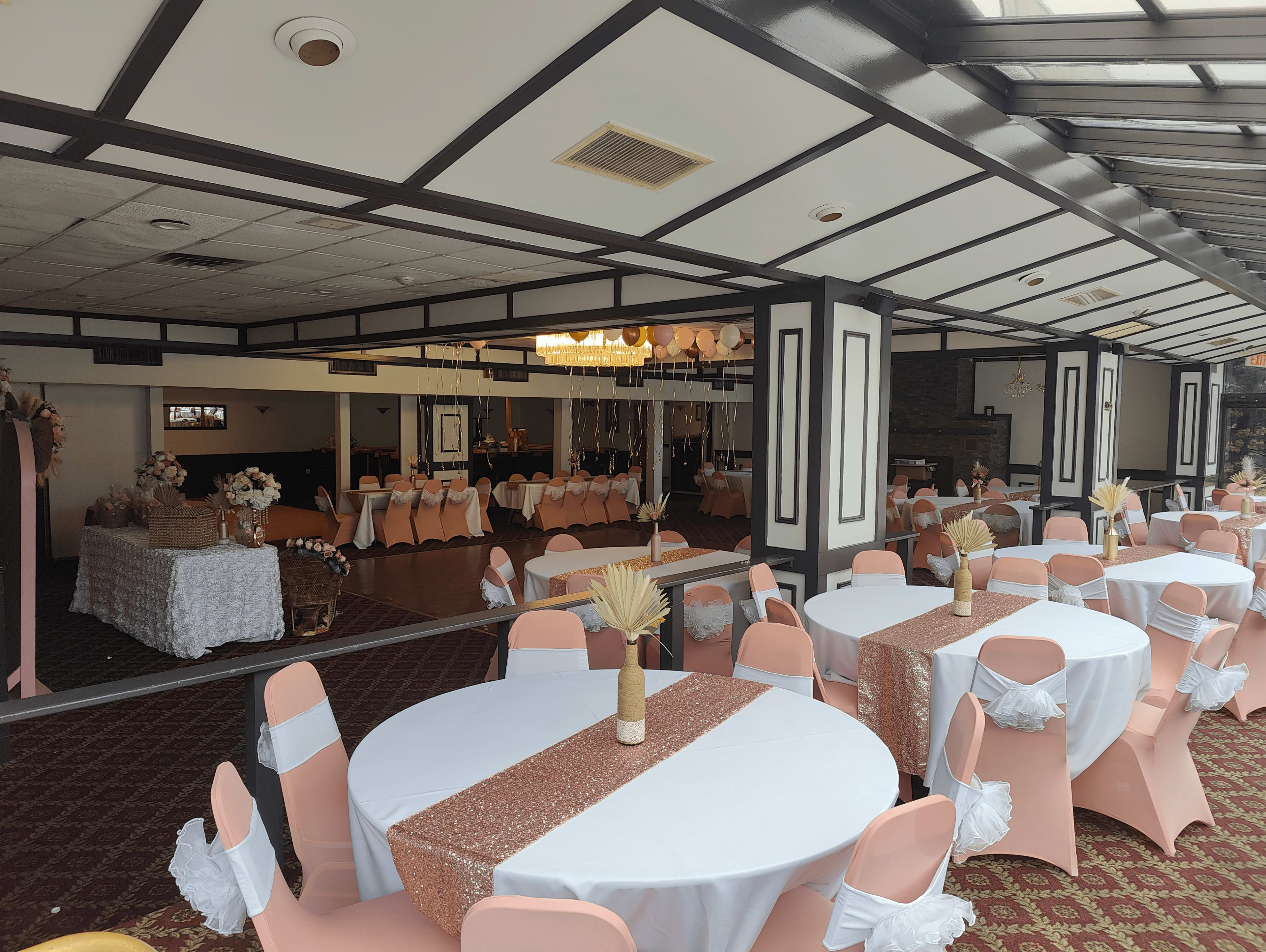 A banquet hall set up for an event, featuring round tables with white tablecloths and pink chairs arranged neatly, along with decorations in the background.