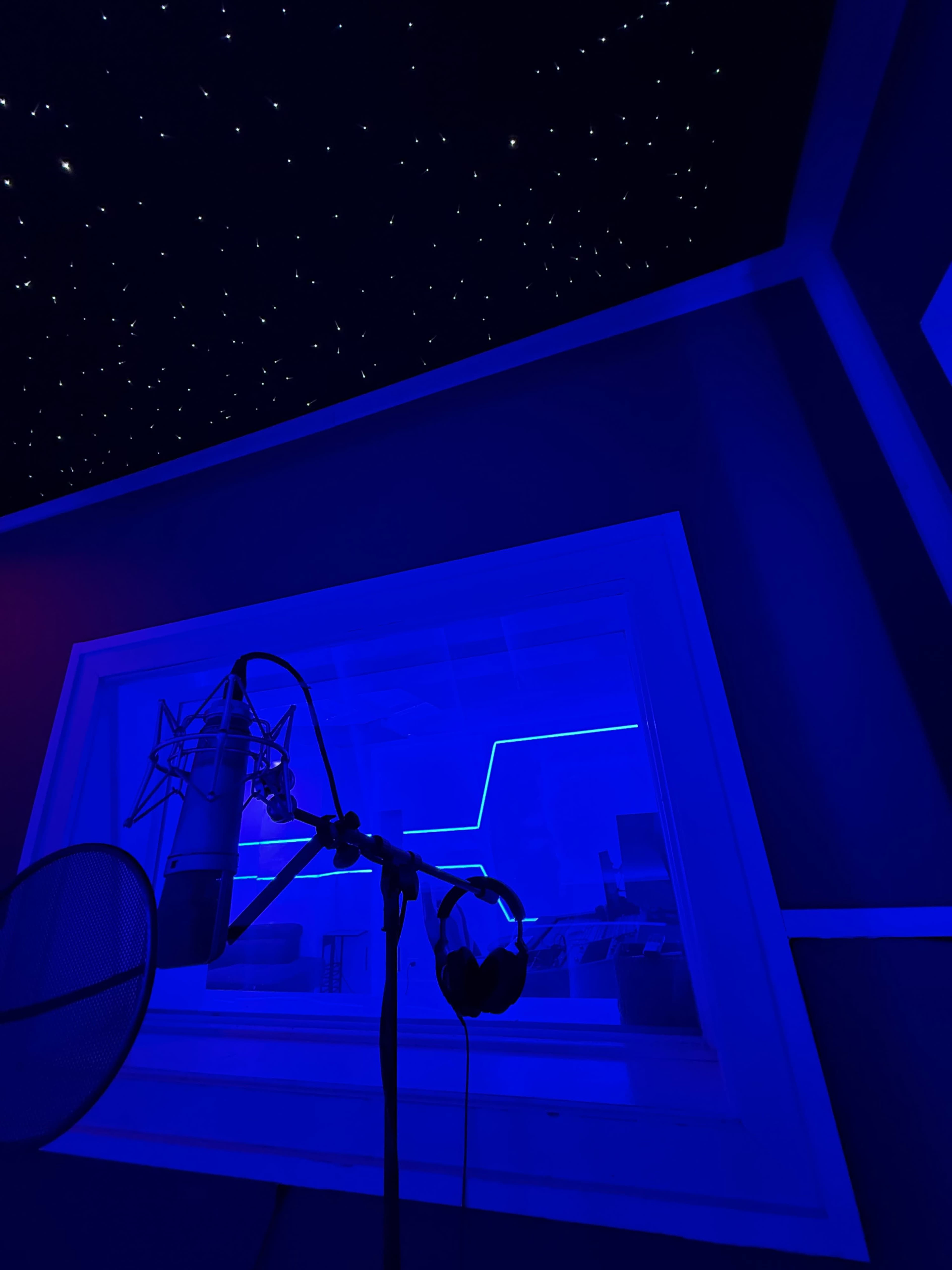 The image shows a recording studio with a microphone, headphones hanging beside it, and a starry ceiling illuminated by blue lights.