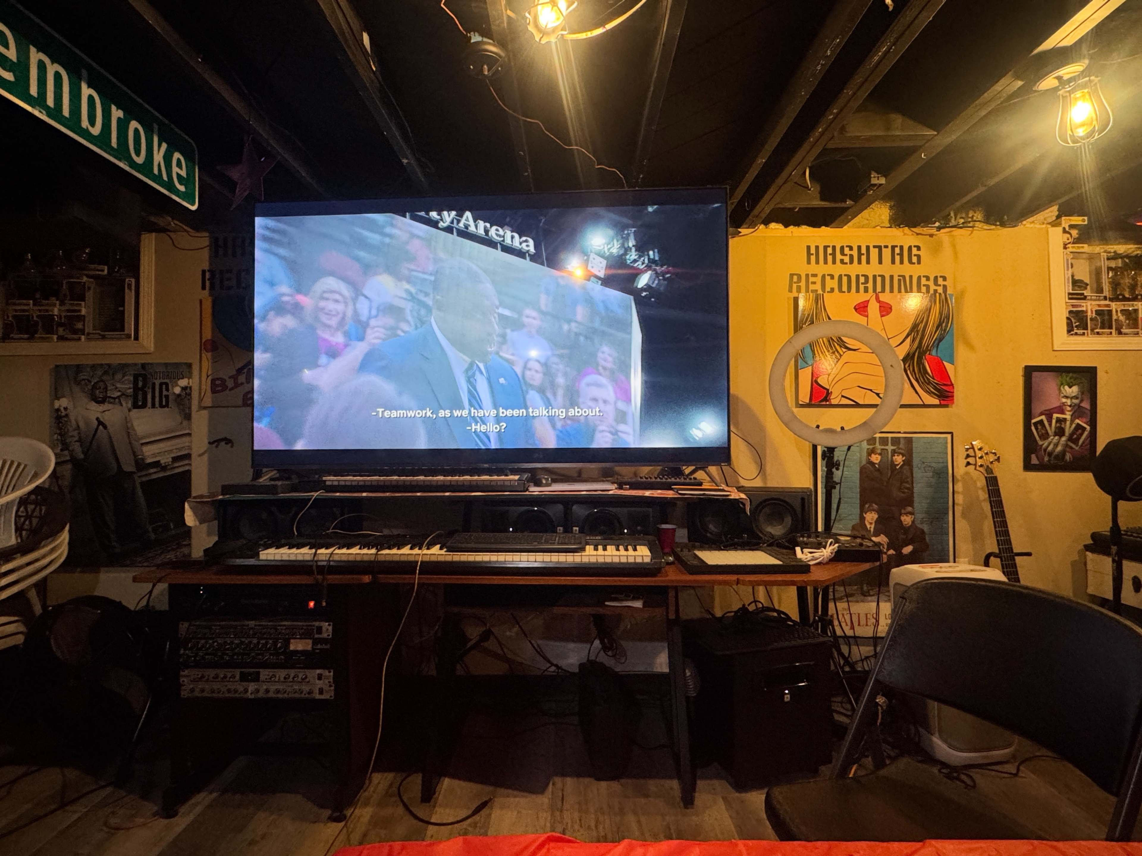 A large television displays a quote about teamwork in a dimly lit basement setting with musical equipment and decorative posters on the walls.