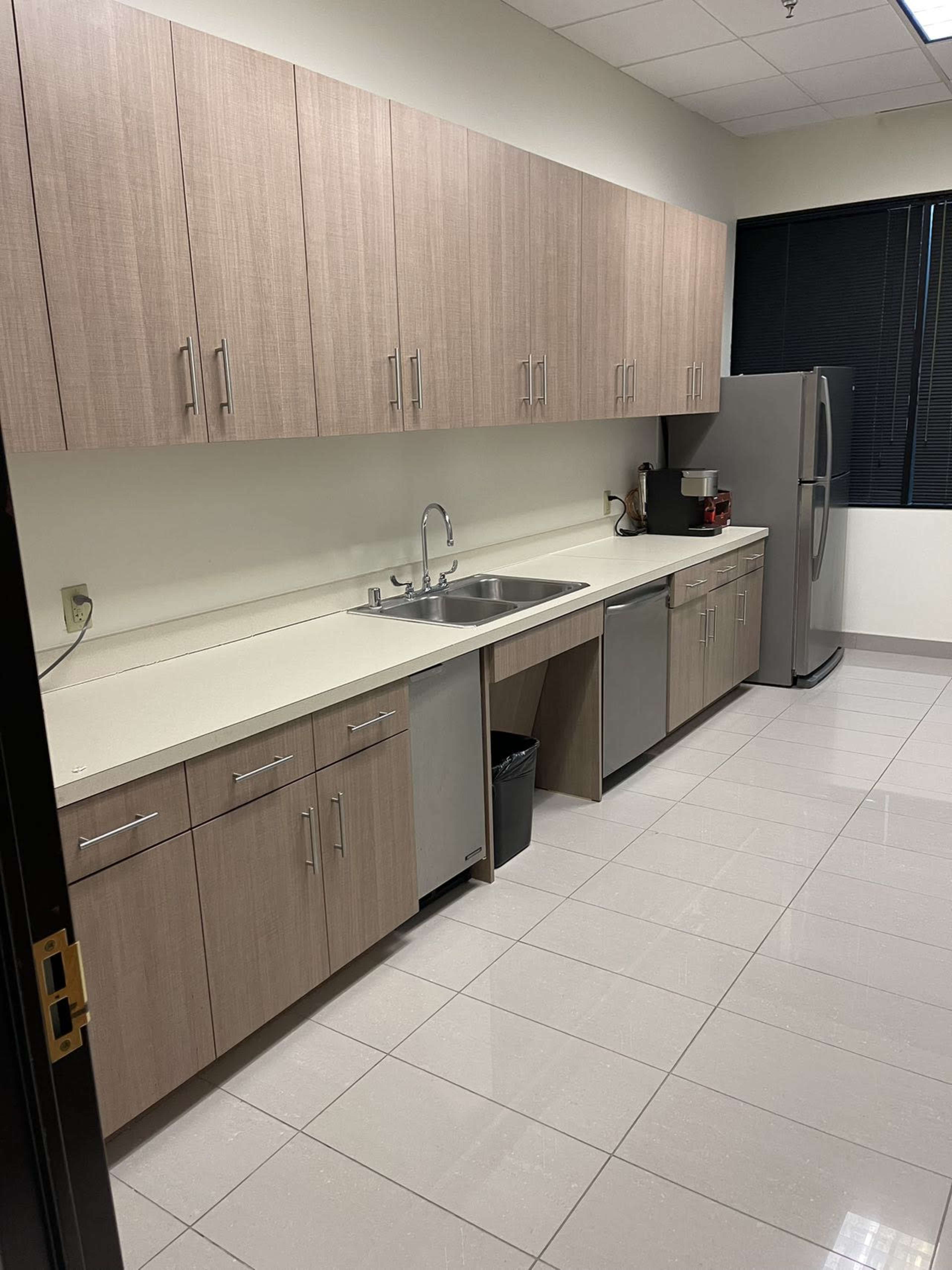 A modern kitchen with beige cabinetry, a sink, stainless steel appliances, and a tiled floor.