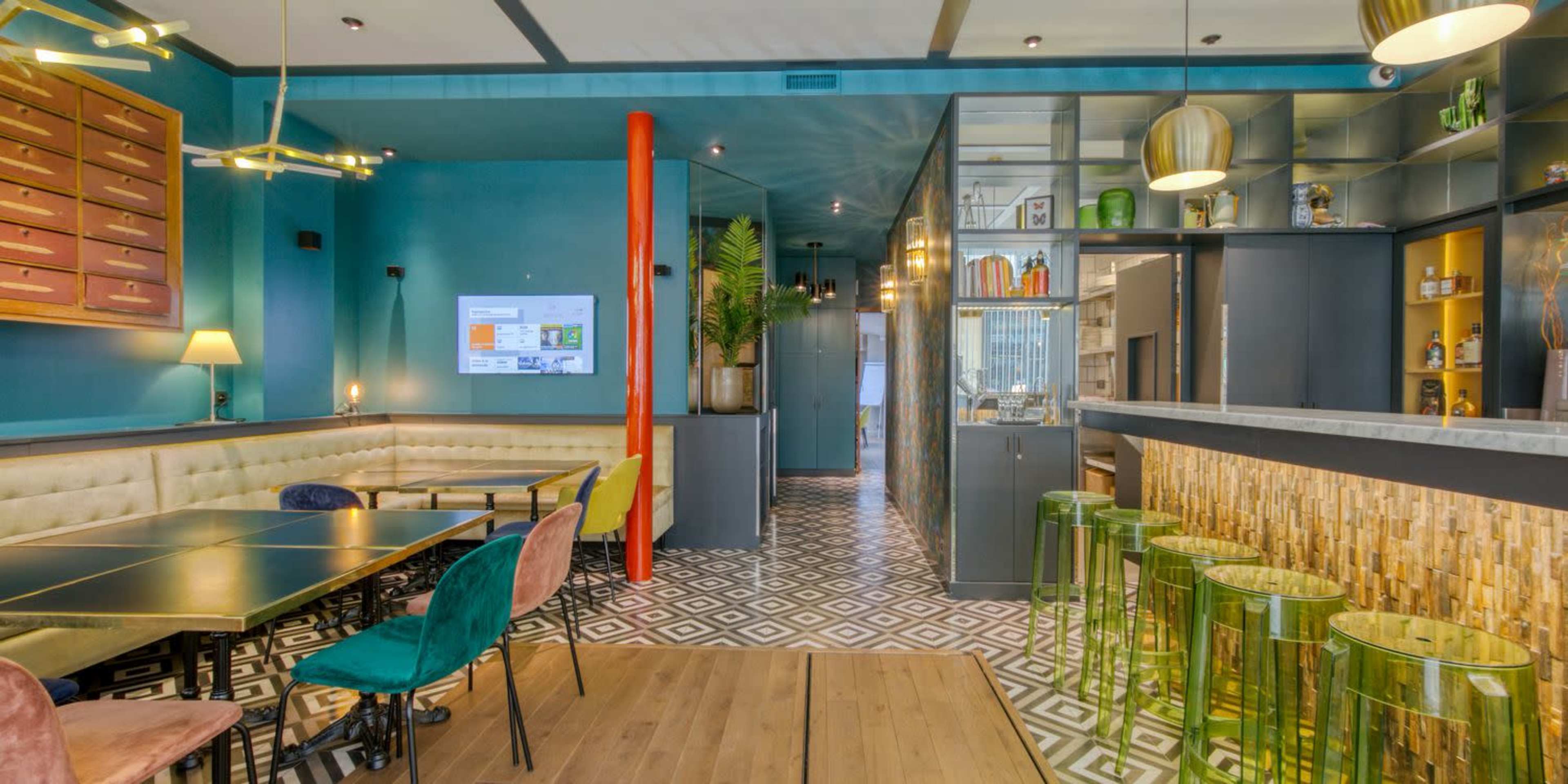 A modern restaurant interior featuring colorful furniture, a bar area with unique stools, and geometric tile flooring.