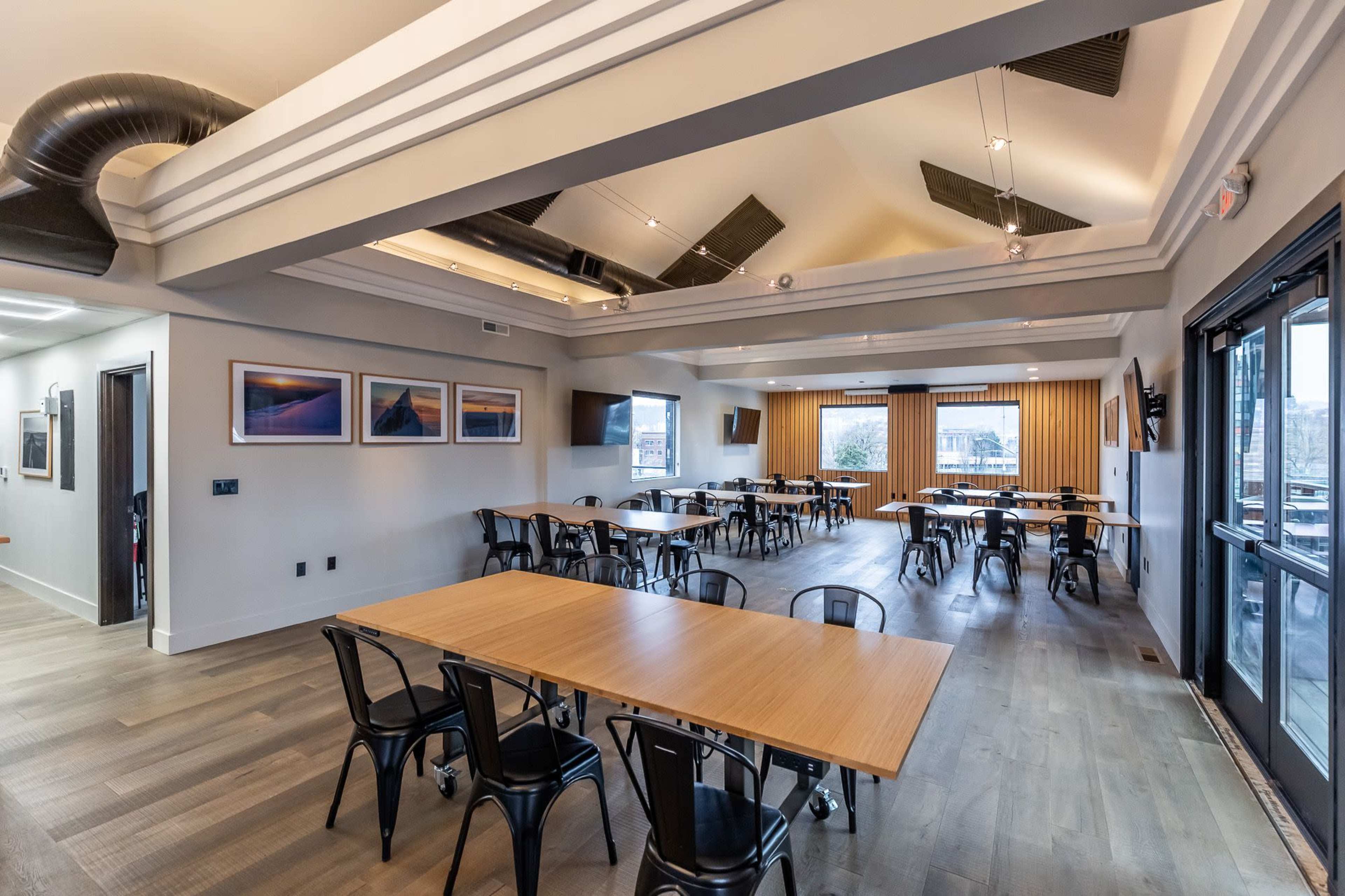 The interior of a spacious restaurant features several tables arranged neatly under a ceiling with modern design elements and large windows that provide natural light.