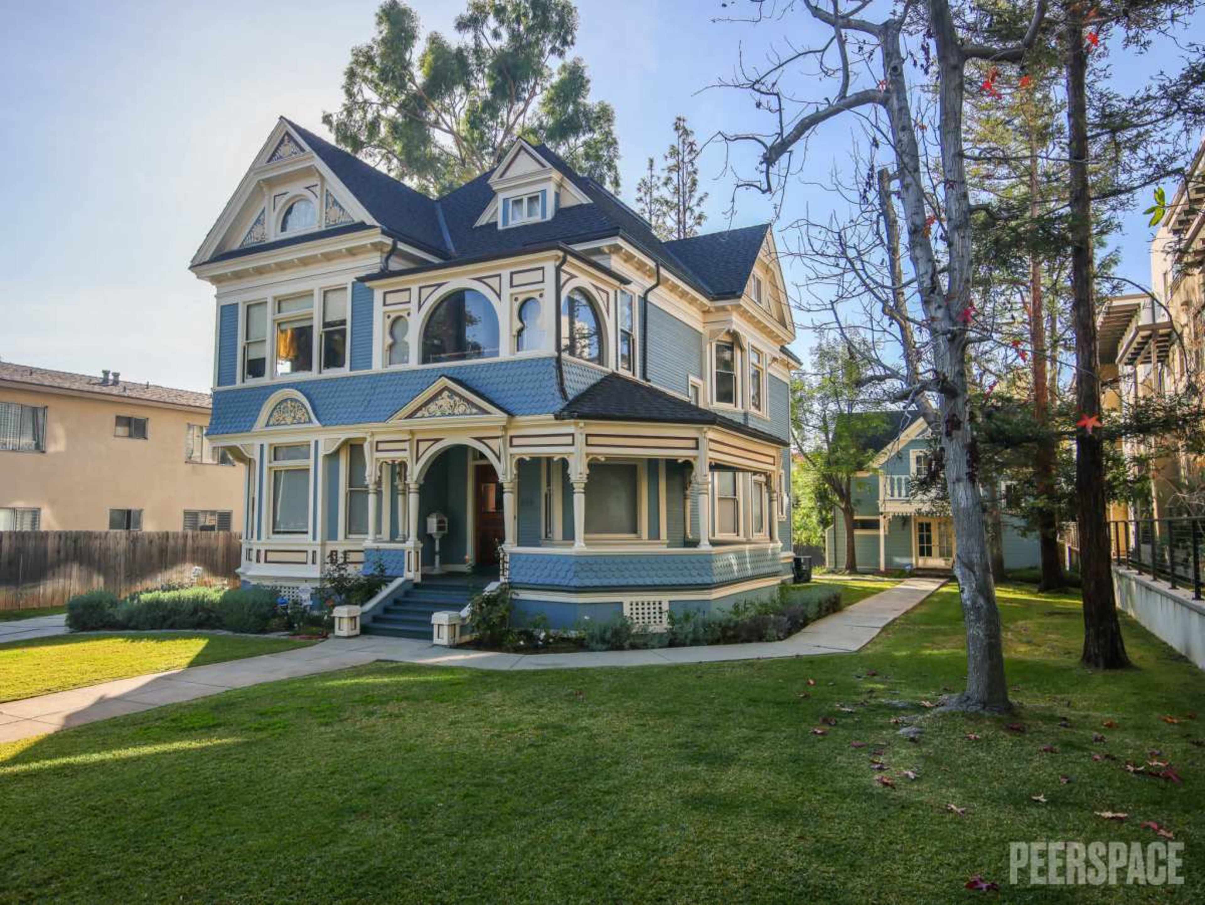 A large Victorian-style house with blue and white exterior trim is surrounded by well-maintained lawns and trees.