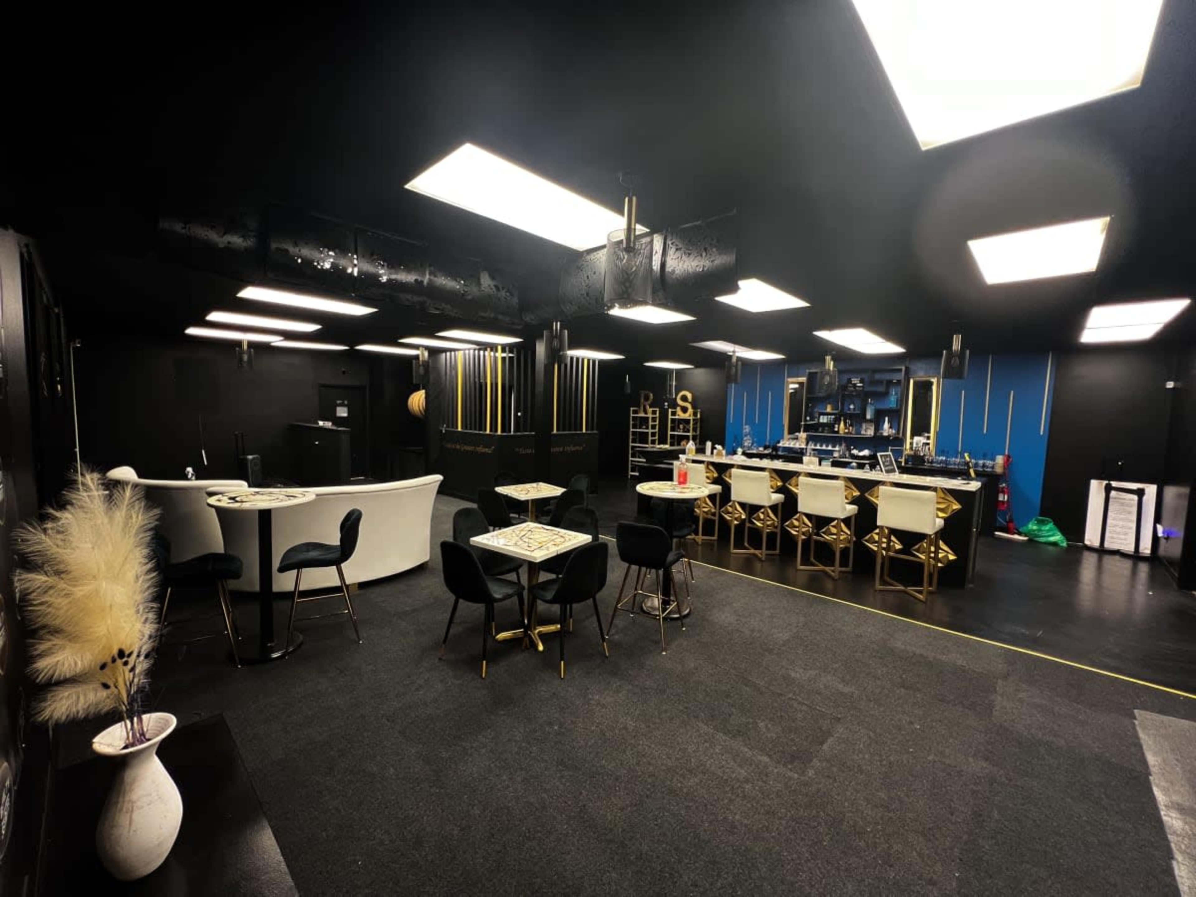 A modern indoor lounge space with black walls, a bar area, and various seating arrangements.