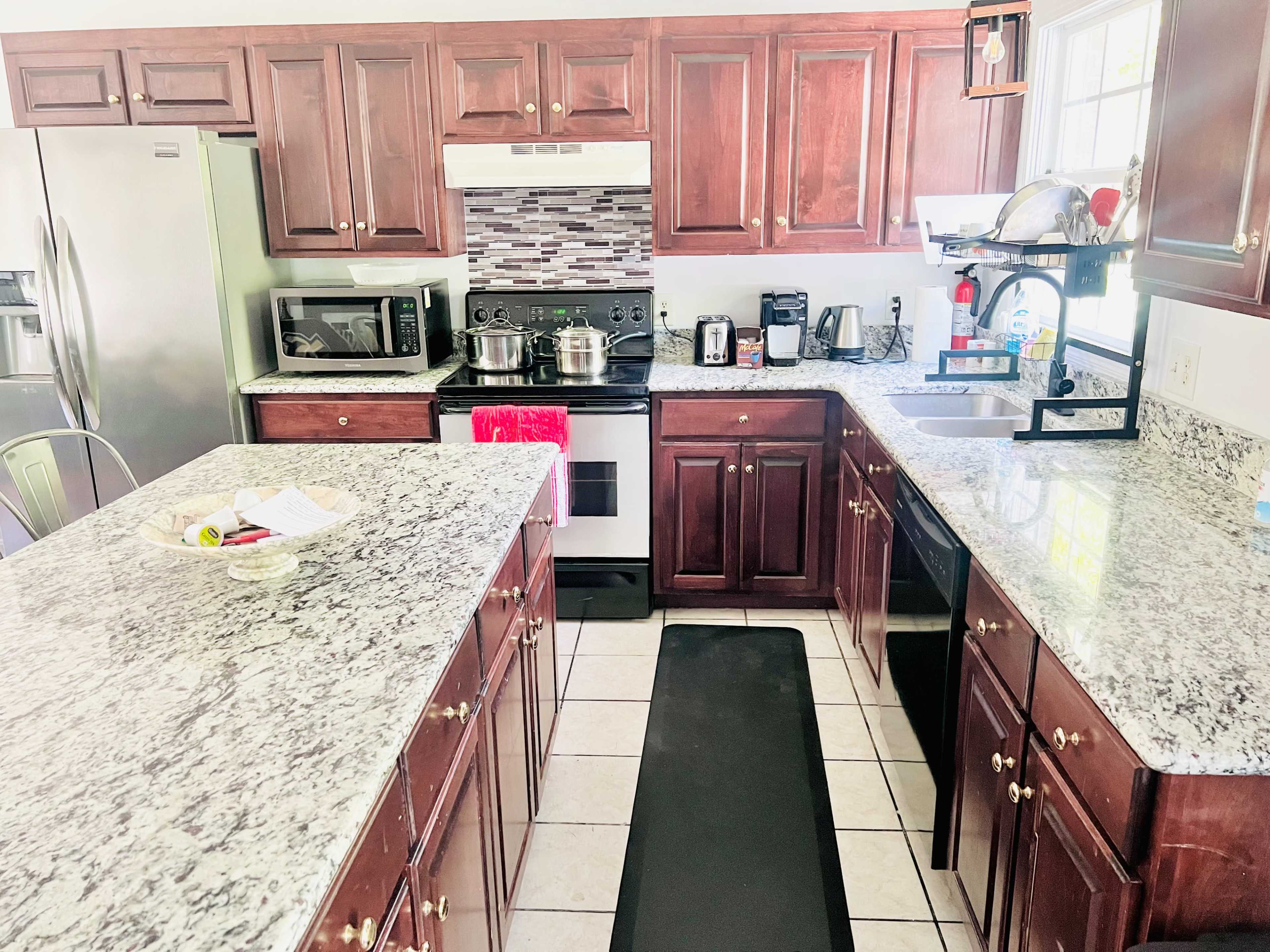 The kitchen features wooden cabinets, granite countertops, and stainless steel appliances arranged around a central island.