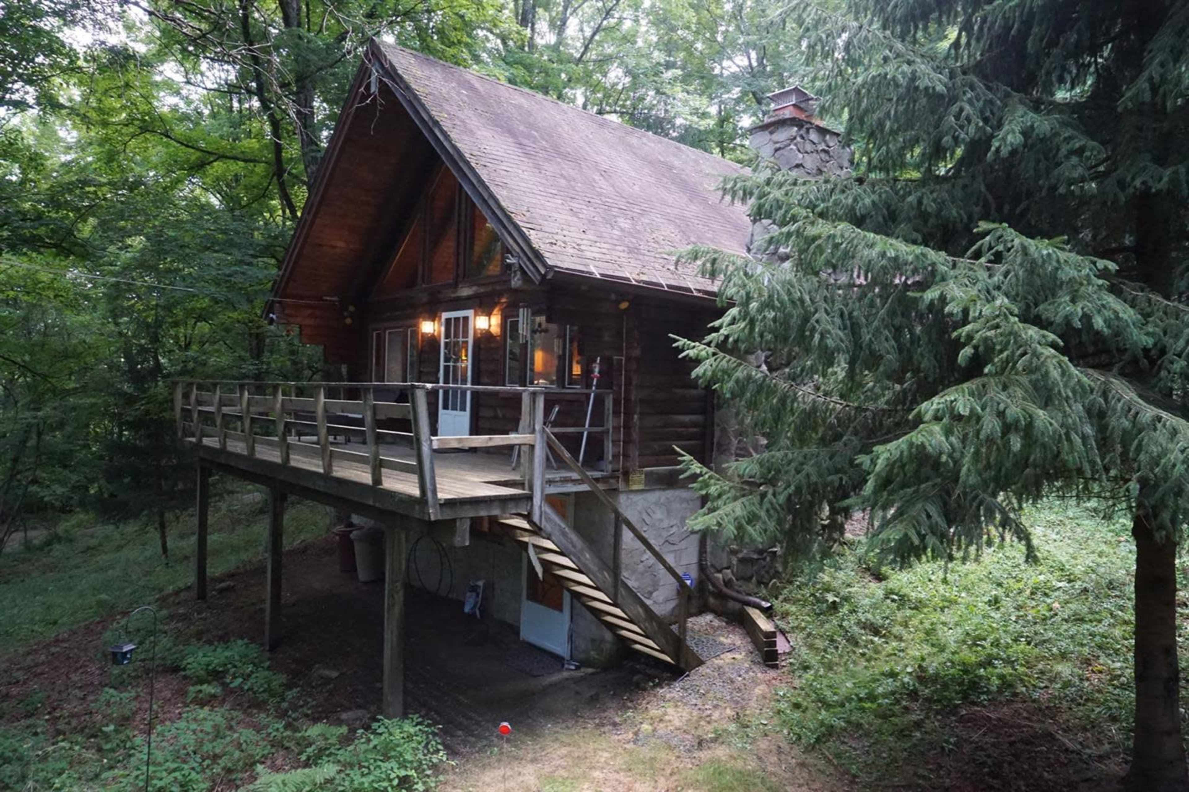 A wooden cabin with a large deck is nestled among trees in a wooded area.