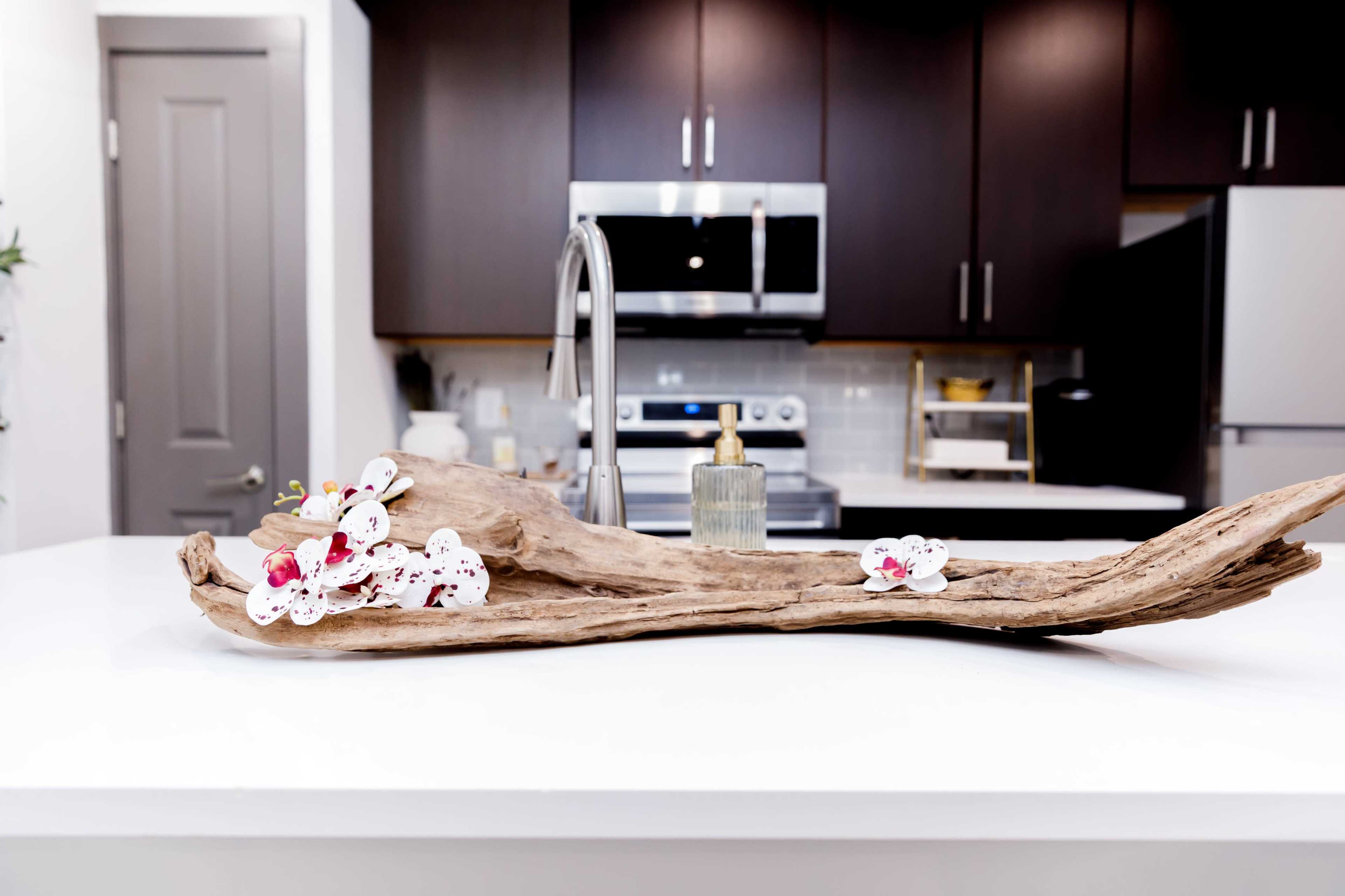 A wooden centerpiece adorned with white orchids rests on a kitchen island, with modern appliances visible in the background.
