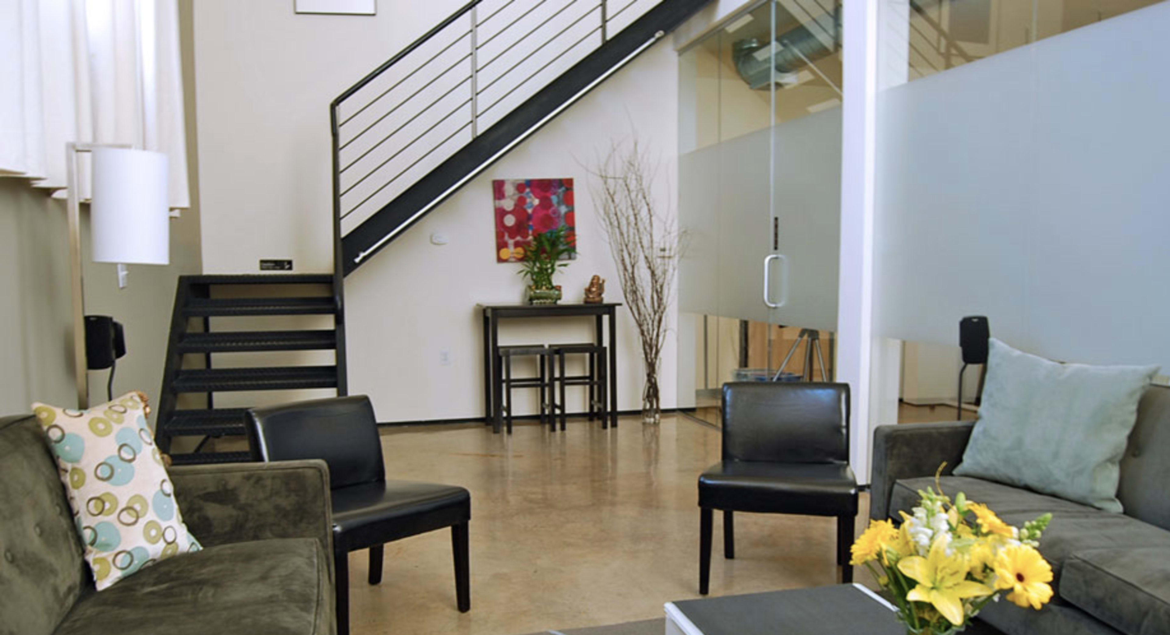 A modern living area with two chairs, a sofa, a coffee table, and a staircase leading to a second floor.