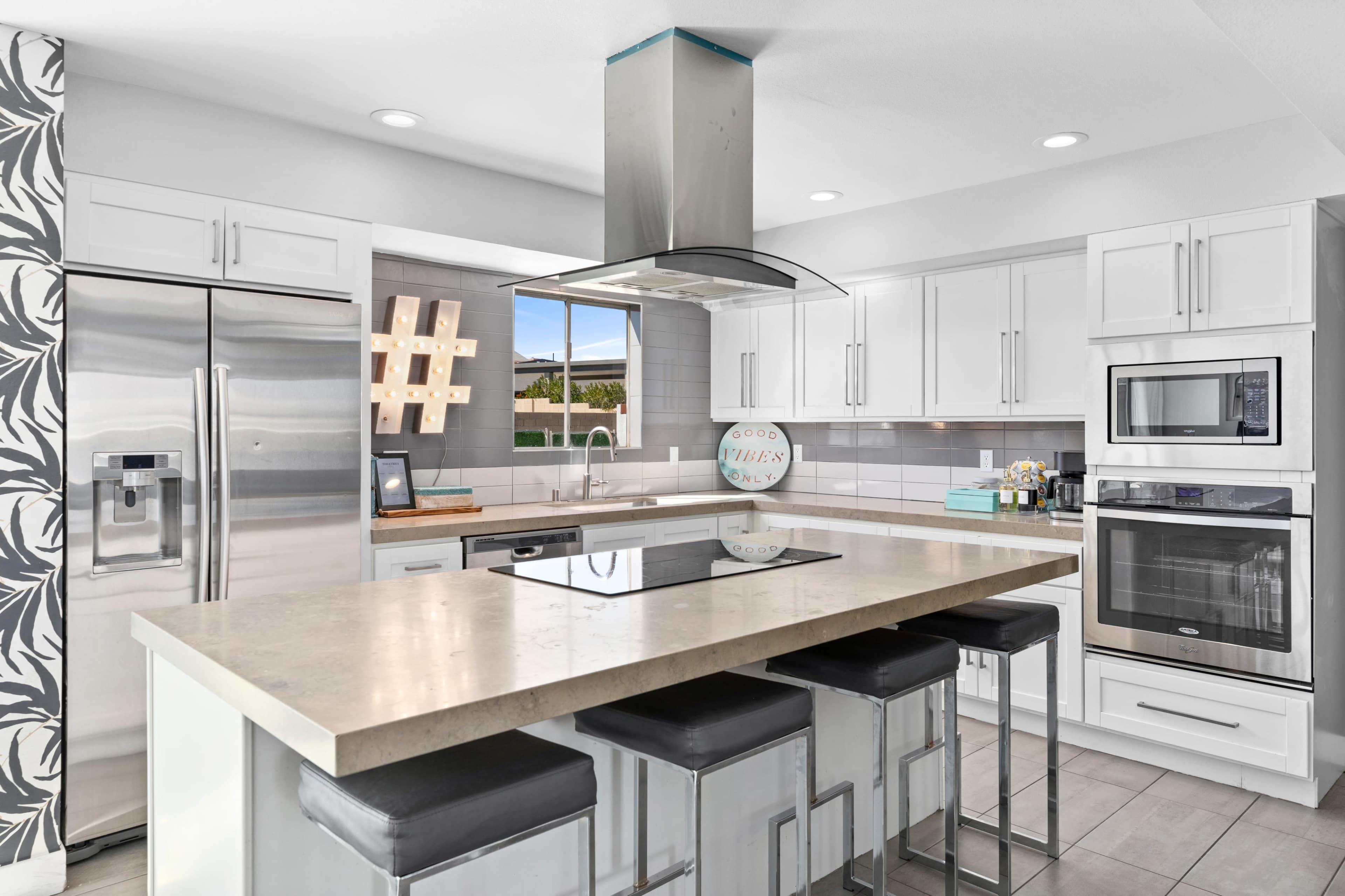 A modern kitchen features white cabinetry, stainless steel appliances, a large island with bar seating, and a window providing natural light.
