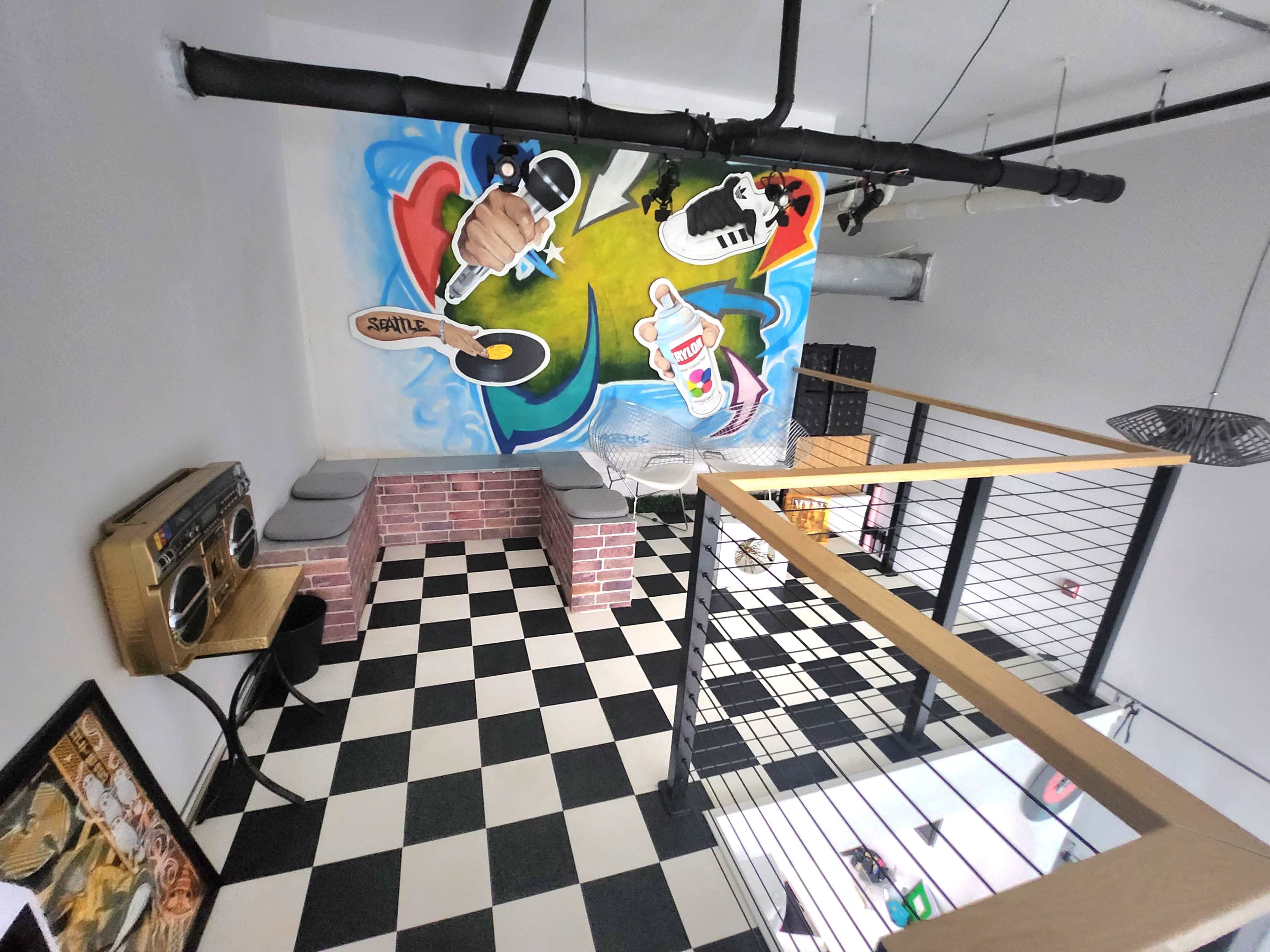 A modern indoor space featuring a checkered floor, a large colorful mural on the wall, a seating area with benches, and a vintage-style audio speaker.