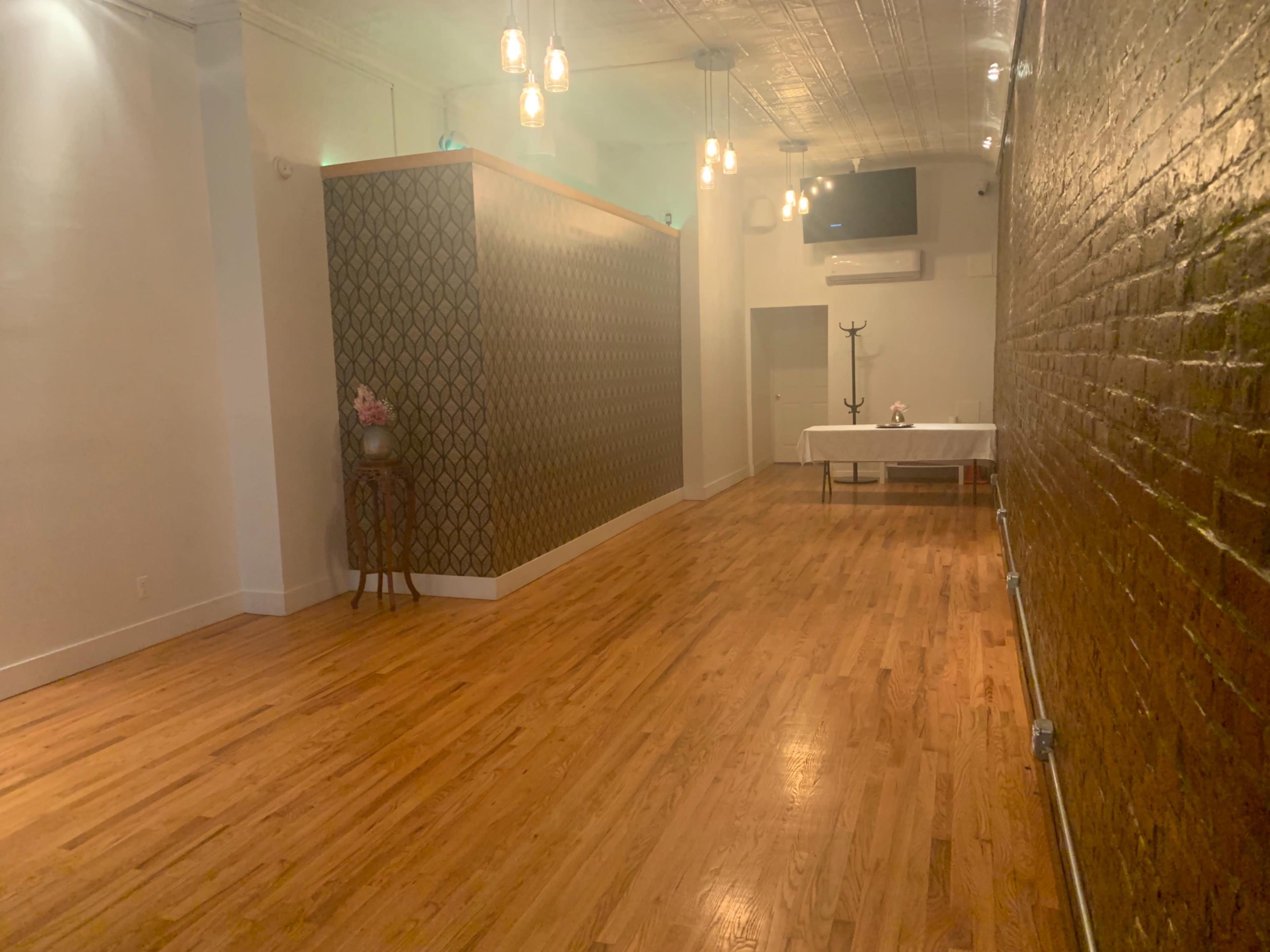 A spacious interior with hardwood floors, a patterned divider wall, a table set up at the end, and pendant lights hanging from the ceiling.