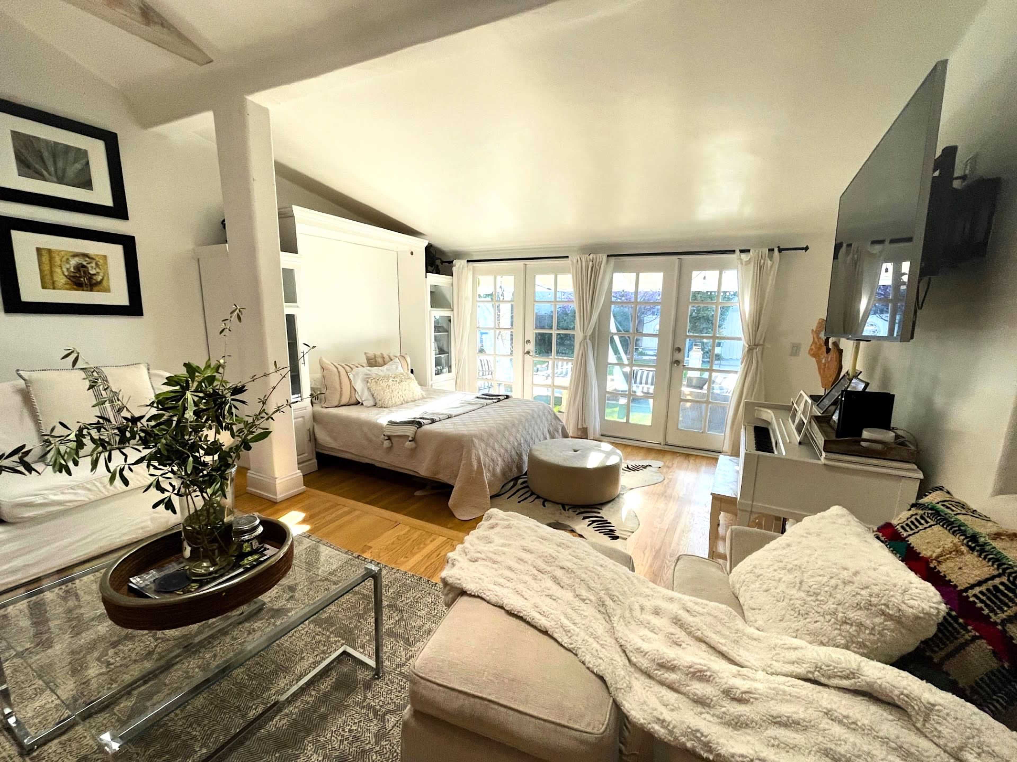 A well-lit bedroom featuring a bed, a seating area with a glass coffee table, and large windows that offer a view outside.