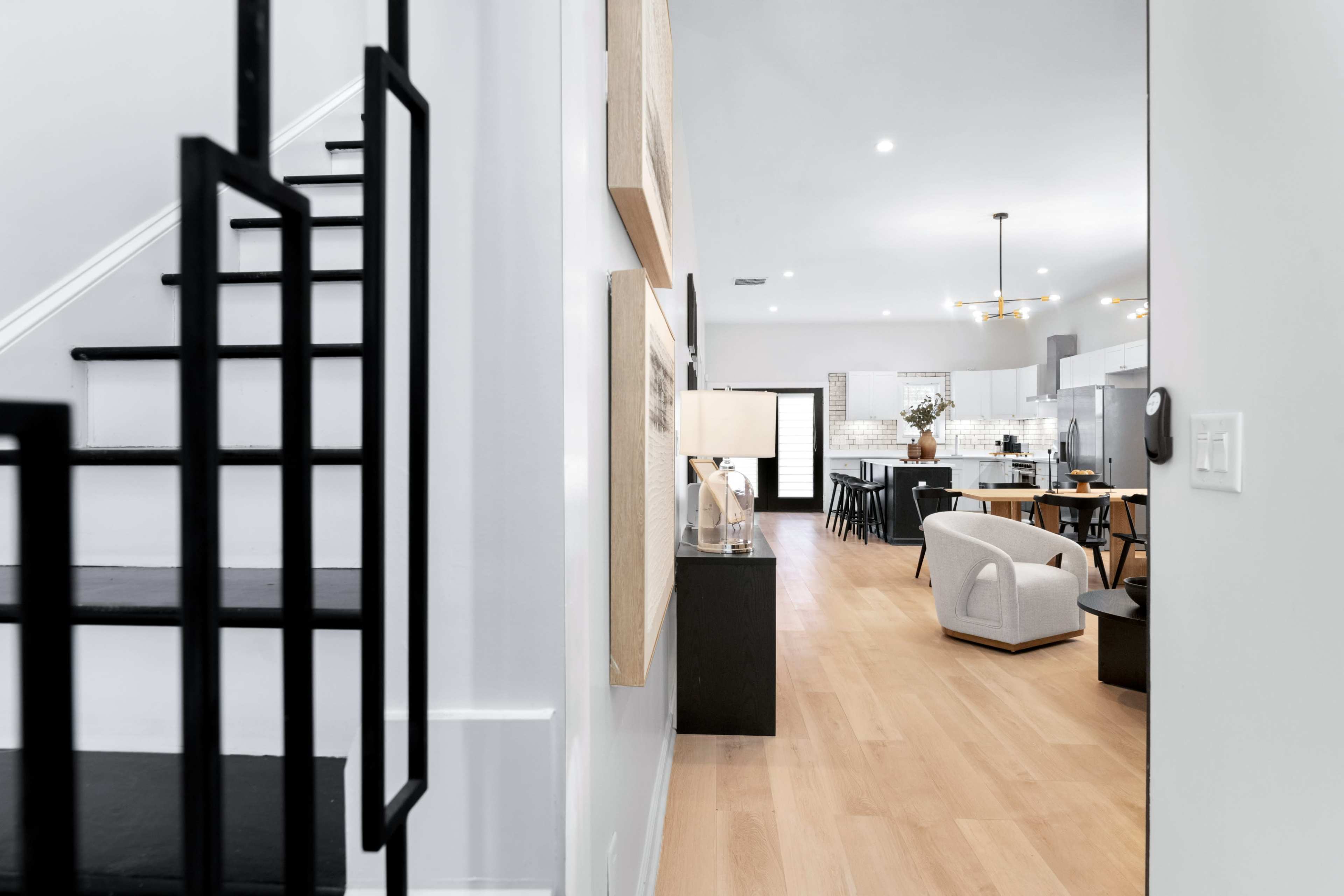 The image shows a modern home interior with a staircase on the left and an open living space featuring a dining area and kitchen in the background.