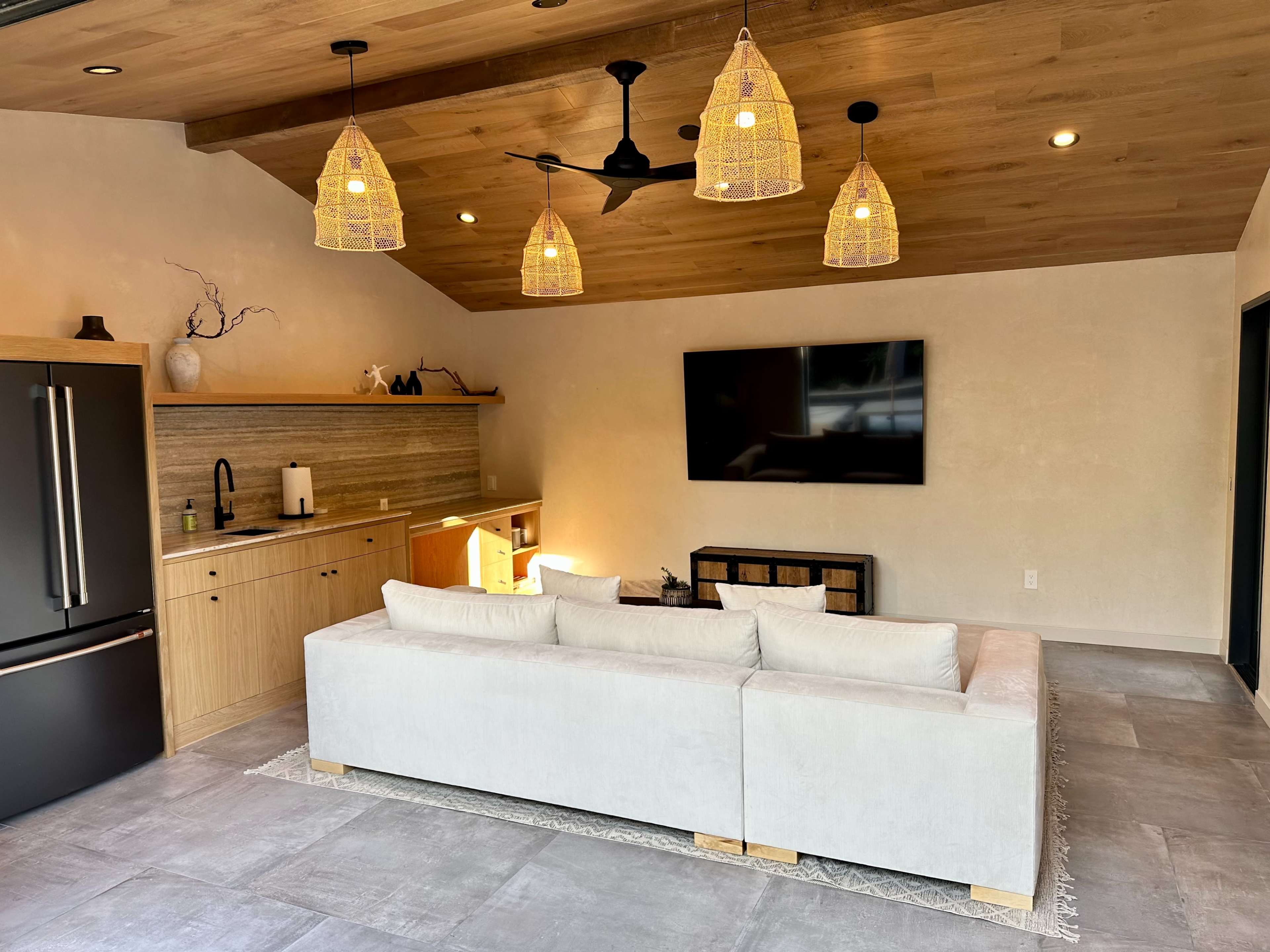 A modern living room features a light-colored sectional sofa, a wooden TV stand, and pendant lighting over a minimalist decor.
