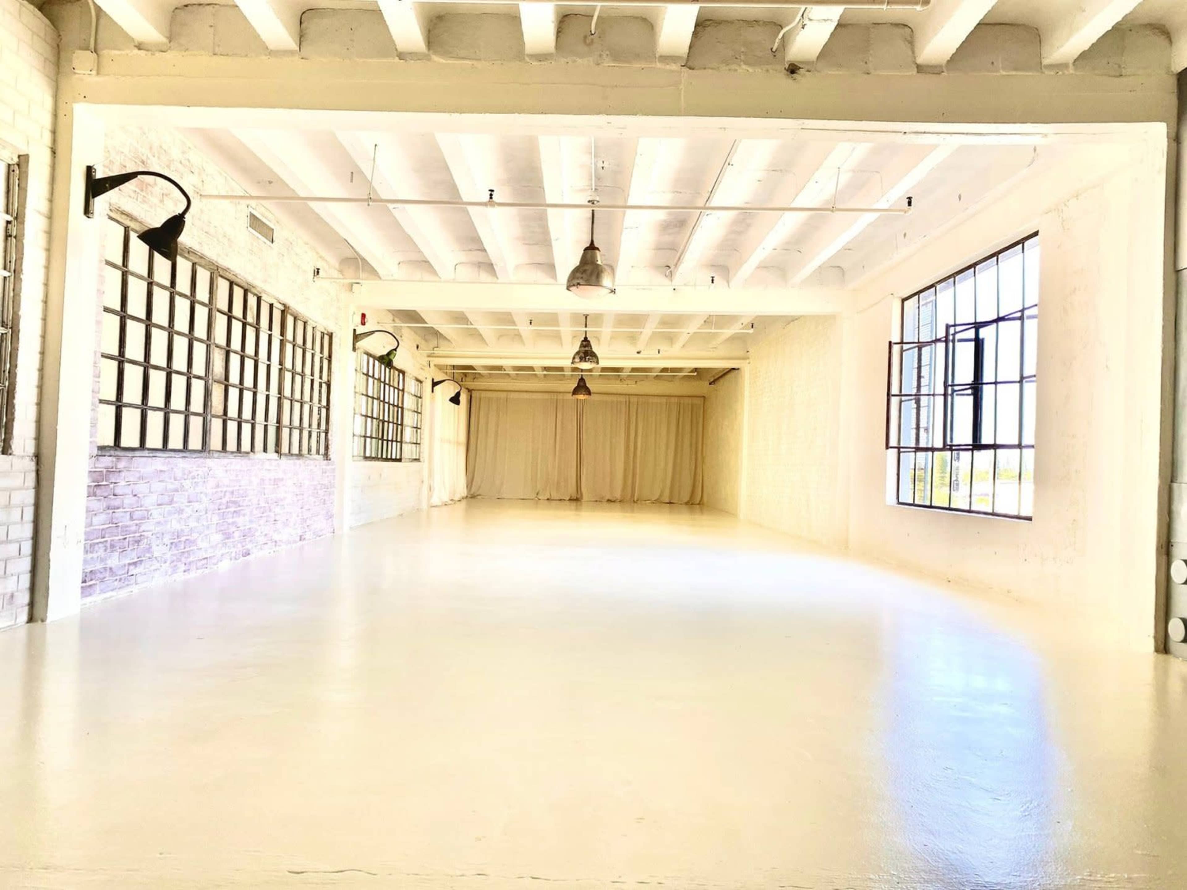 A spacious, well-lit room featuring white walls, high ceilings, and large windows.