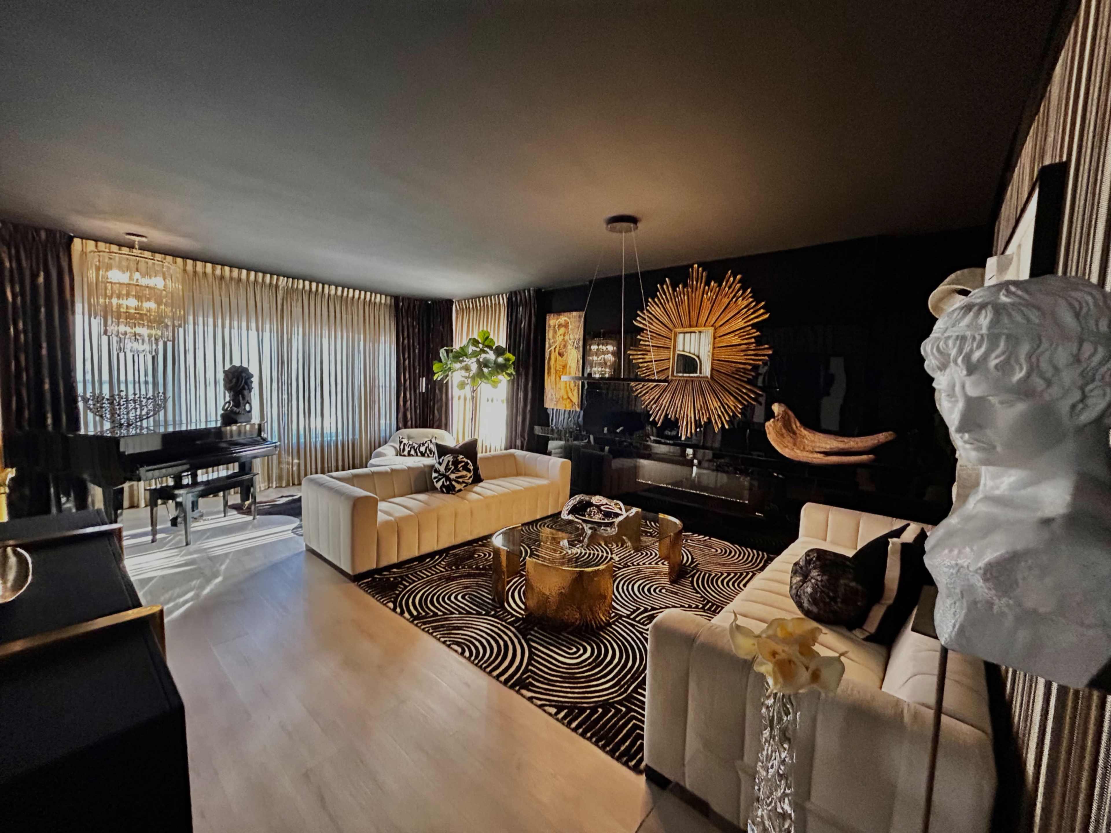 The image shows a modern living room featuring white couches, a black and white patterned rug, and a large decorative mirror on the wall, with ample natural light coming through the curtains.