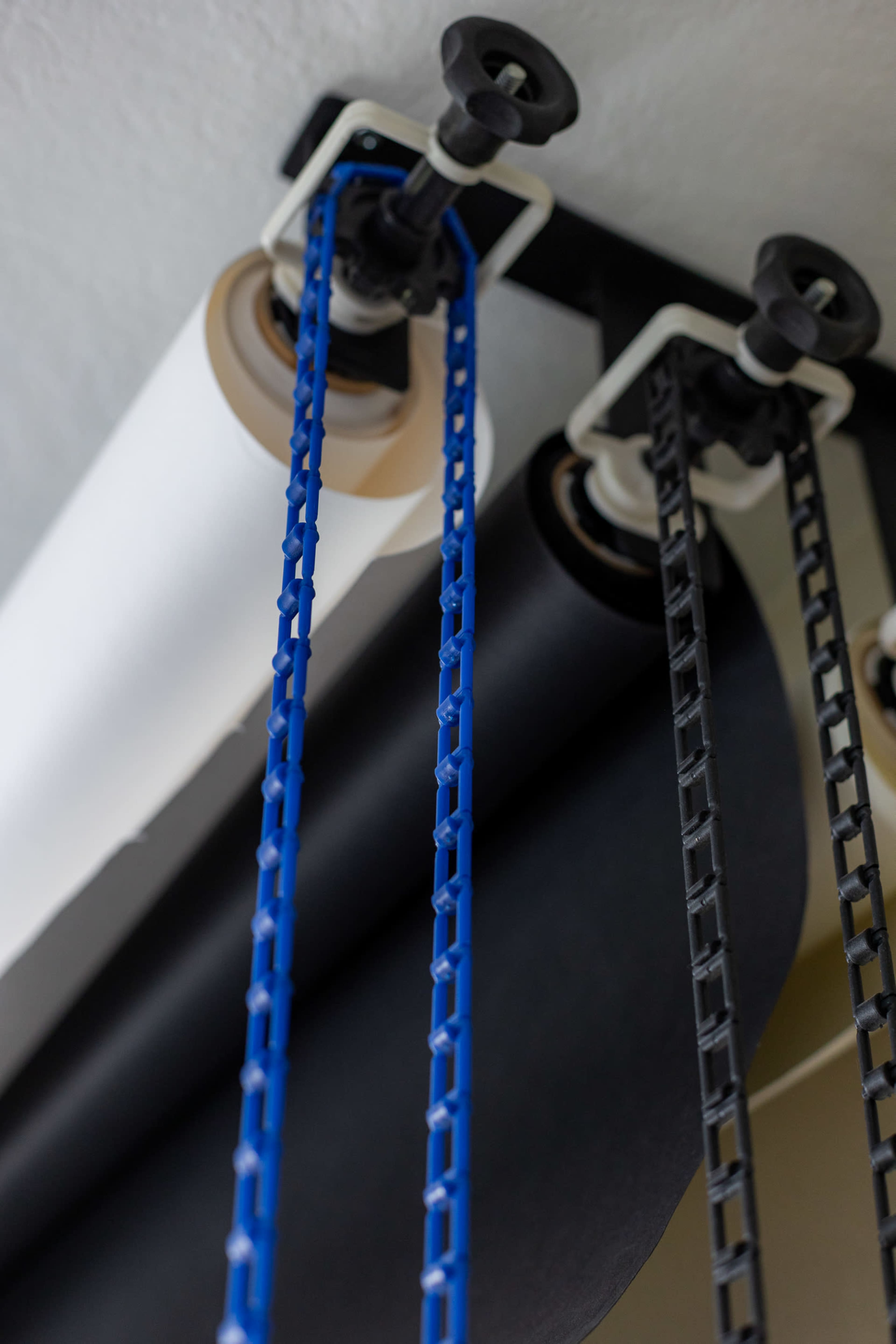 A rolling system with three different colored paper rolls: white, black, and a blue chain mechanism.